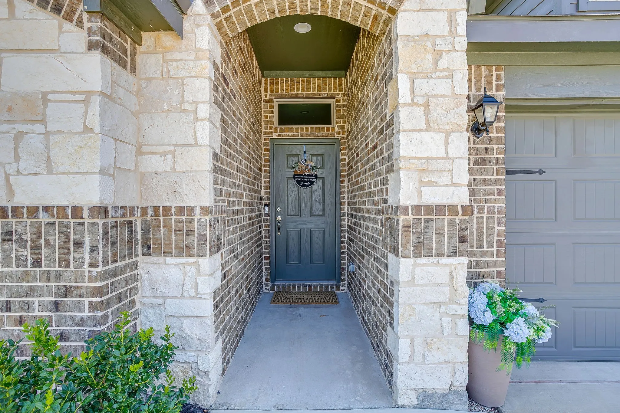 Brick and stone exterior with an arched entryway, featuring a paneled door with transom window, and an attached garage with carriage-style hardware