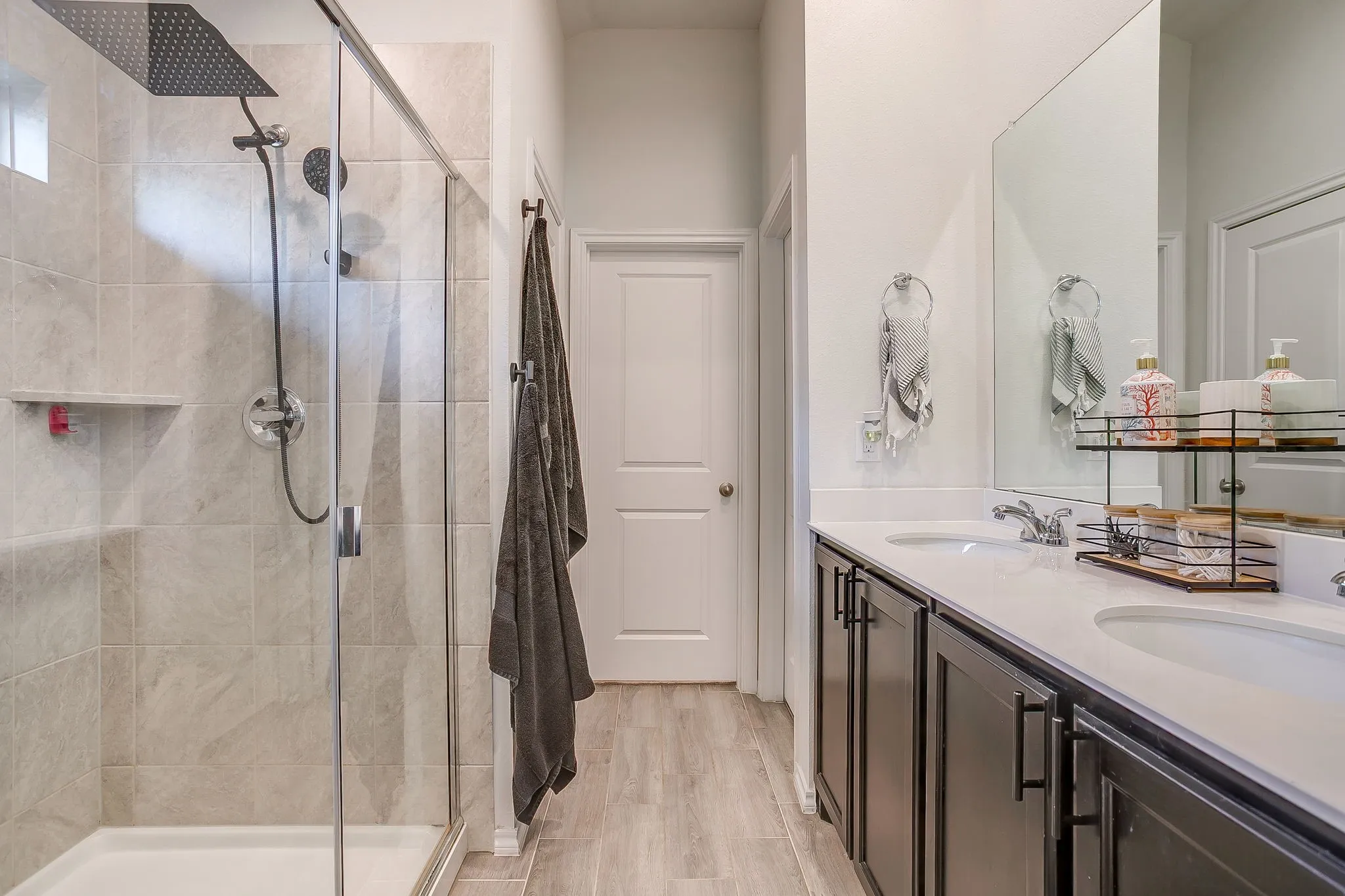 Tiled shower with a rainfall showerhead, dual vanity with undermount sinks, and dark wood-finish cabinetry