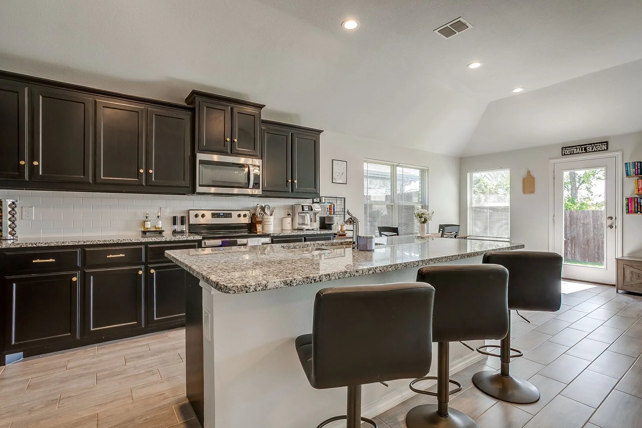 Kitchen featuring dark cabinetry, stainless steel appliances, a tile backsplash, and a granite-finish island