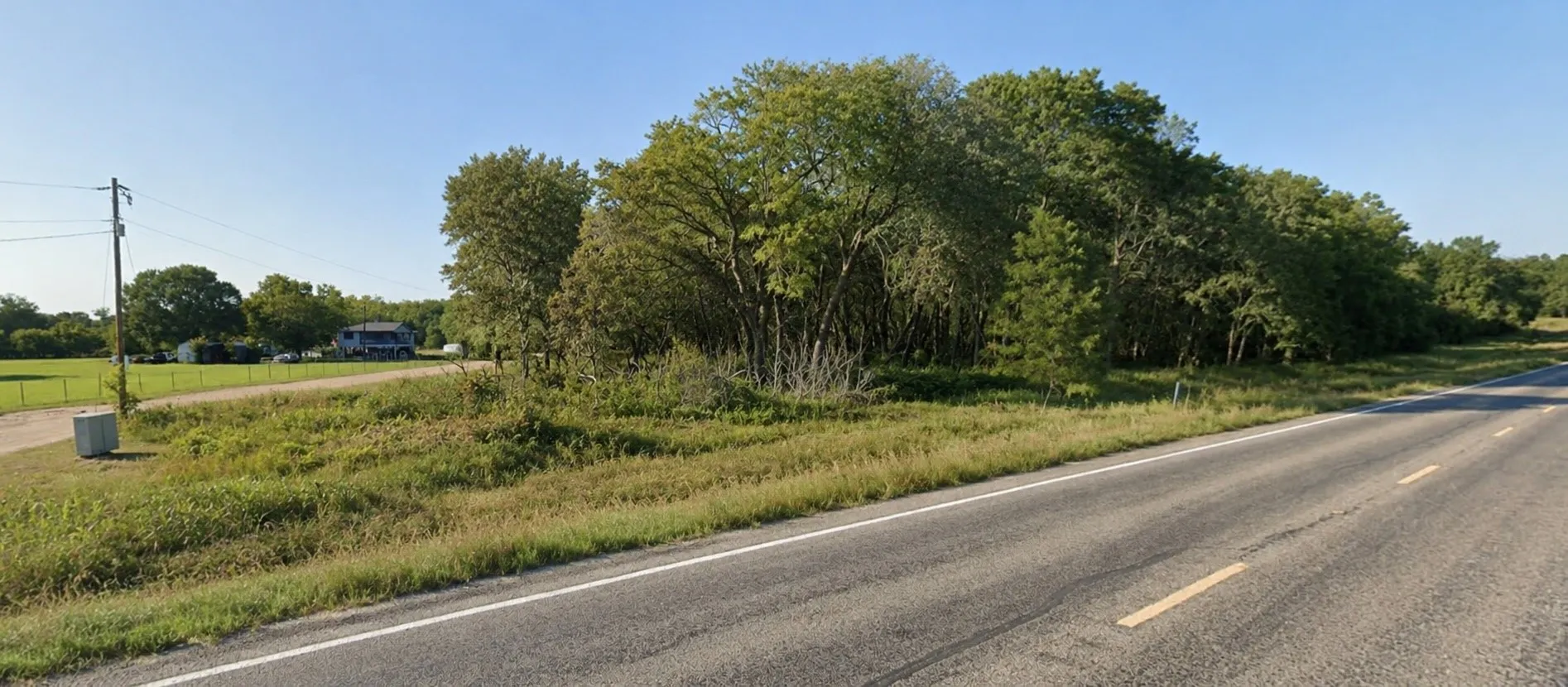 Expansive land parcel featuring a paved road frontage, utility pole at the street.