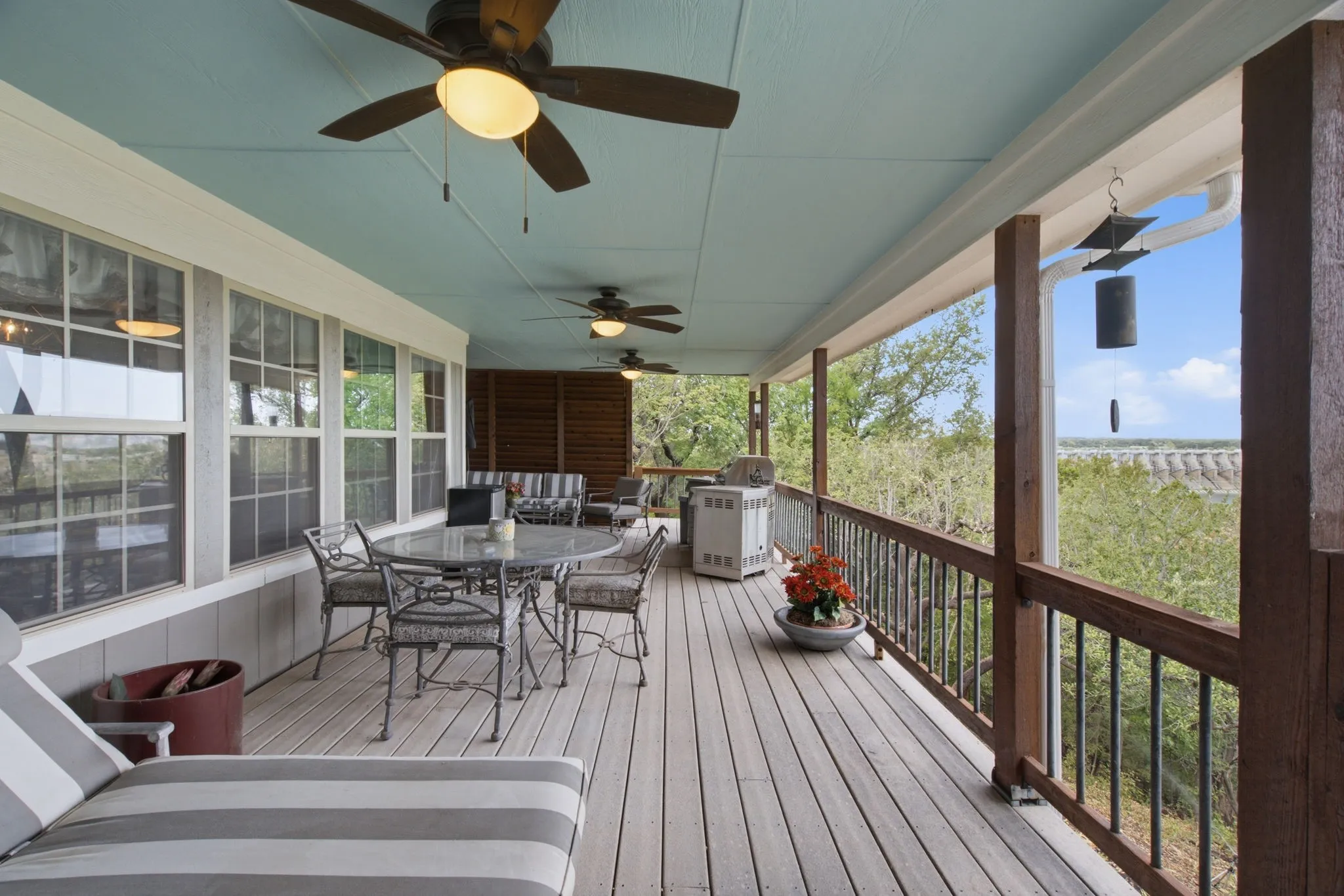 Expansive outdoor deck with wood-finish flooring, protective railing, and multiple ceiling fans