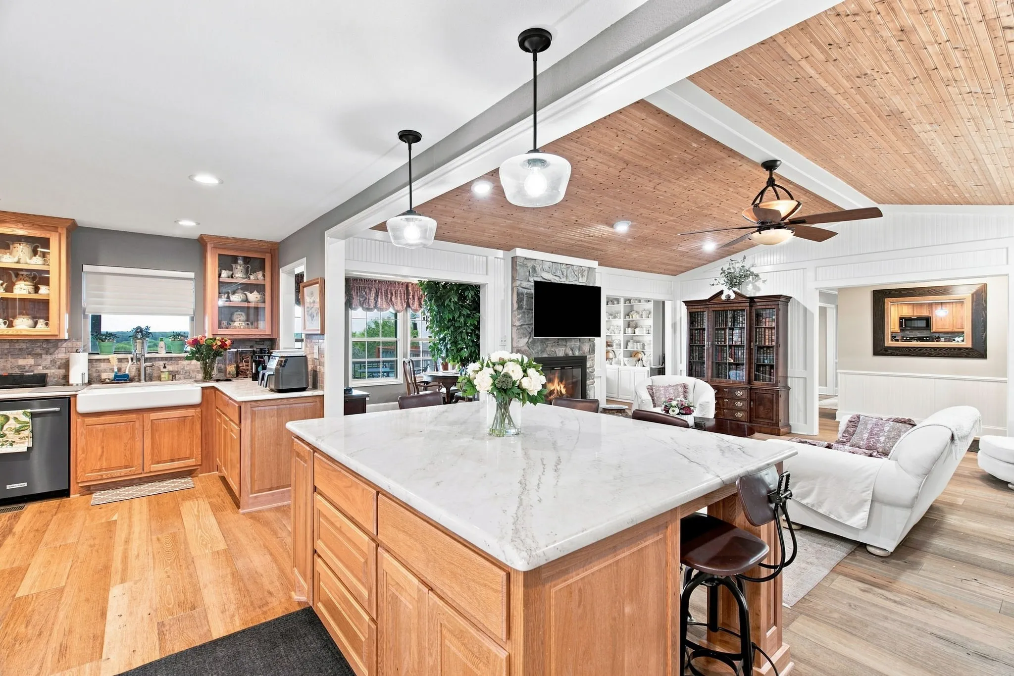 Expansive kitchen island with a light-toned countertop, wood cabinetry, apron-front sink, and wood-finish flooring