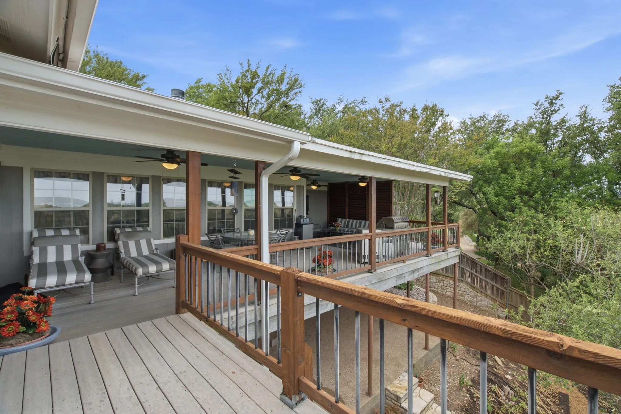 Expansive outdoor deck with wood railing, covered patio area with ceiling fans and recessed lighting, and a wall of windows