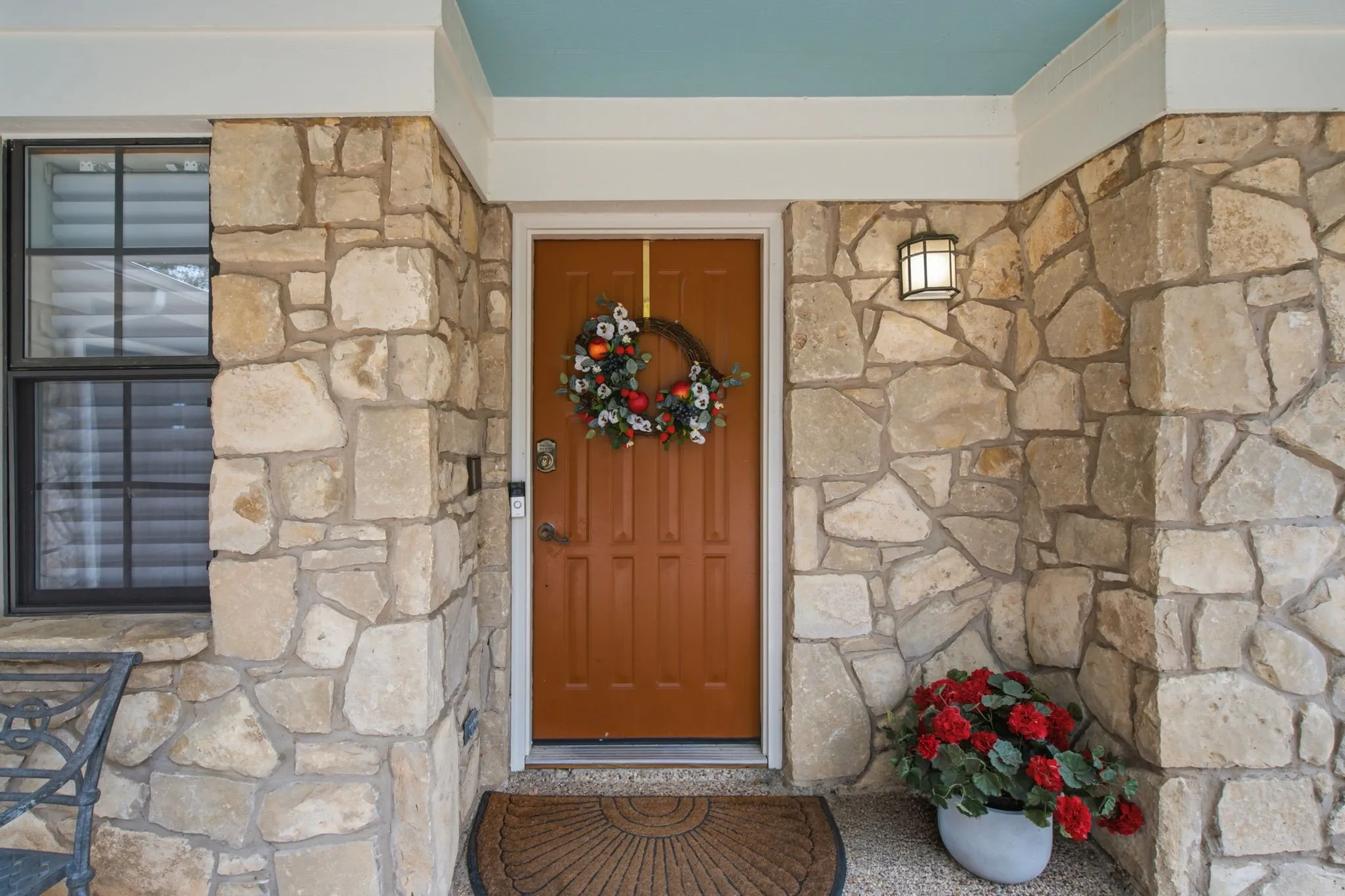 Stone facade with a prominent entry door, an exterior wall-mounted light fixture, and a window with blinds