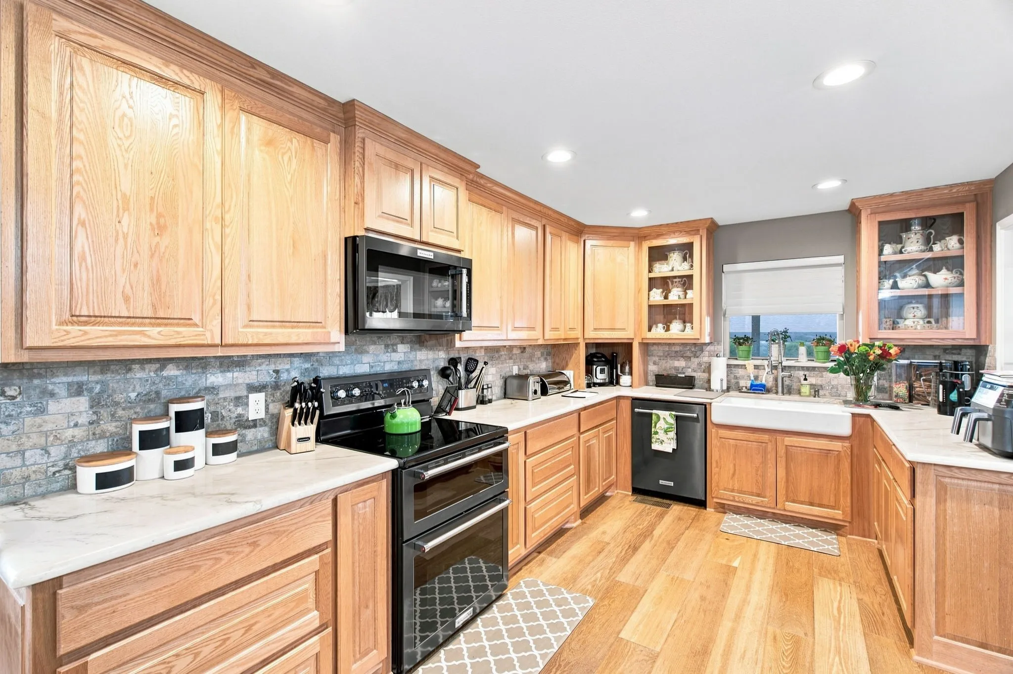 Light wood-finish cabinetry, quartz countertops, tile backsplash, built-in black microwave, and black electric range with double ovens
