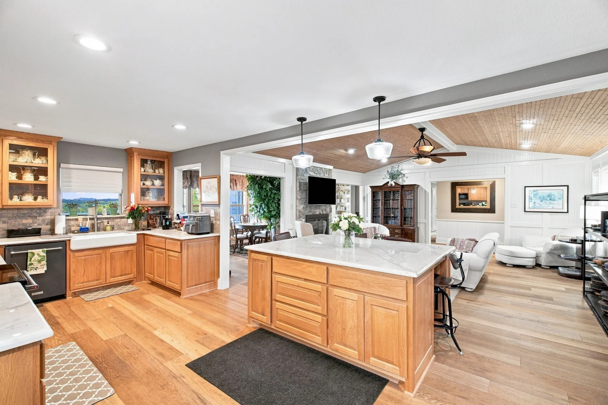 Open-concept kitchen and living area featuring wood-finish flooring, a kitchen island with stone countertop, natural wood cabinetry, and a shiplap ceiling in the living space