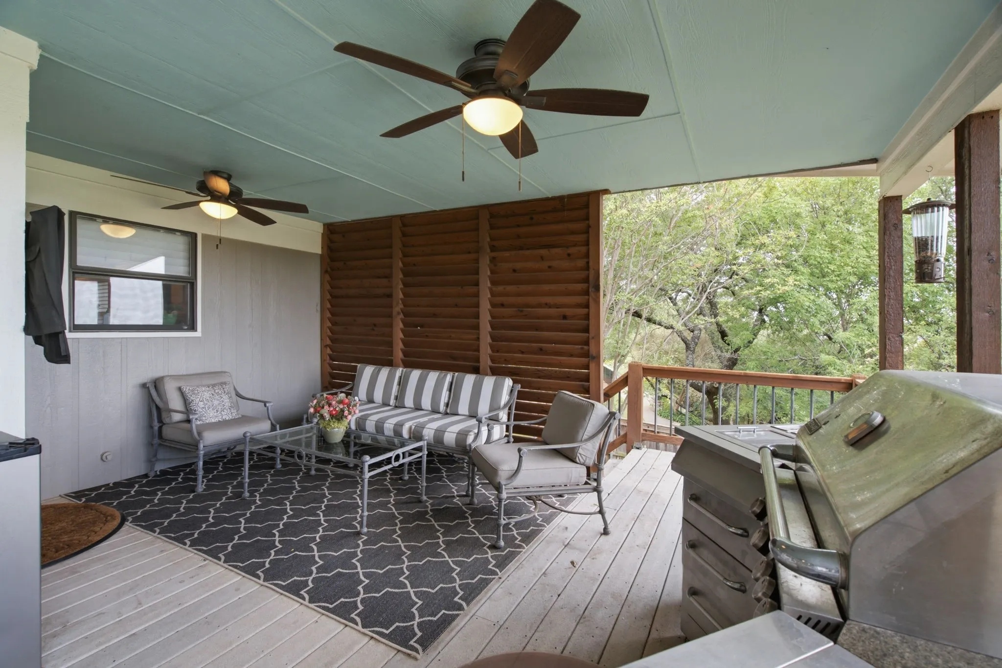 Expansive covered deck featuring wood-finish flooring, a full-height privacy screen, and dual ceiling fans