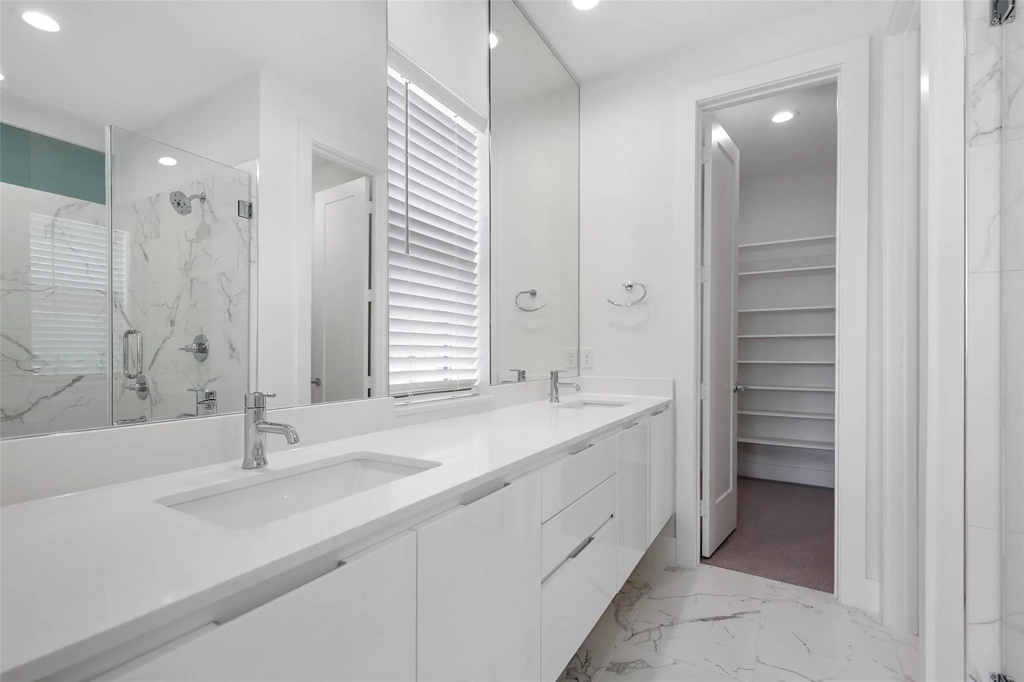 Dual vanity with integrated sinks, chrome fixtures, large mirror, glass-enclosed shower, and built-in shelving