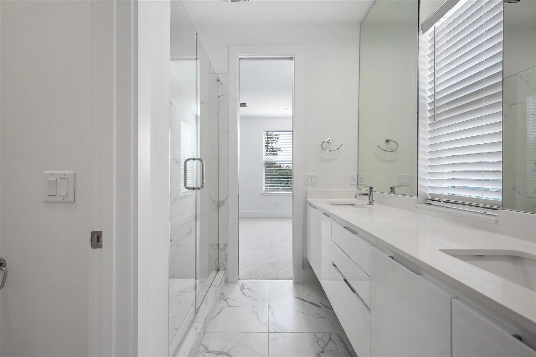 Dual vanity with undermount sinks, frameless glass shower enclosure, and large format marble-look tile flooring