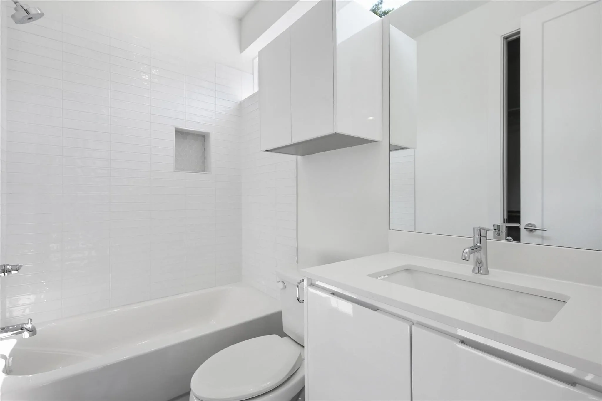 White subway tile shower surround with recessed niche, integrated bathtub, sleek white vanity with undermount sink, and wall-mounted mirrored medicine cabinet