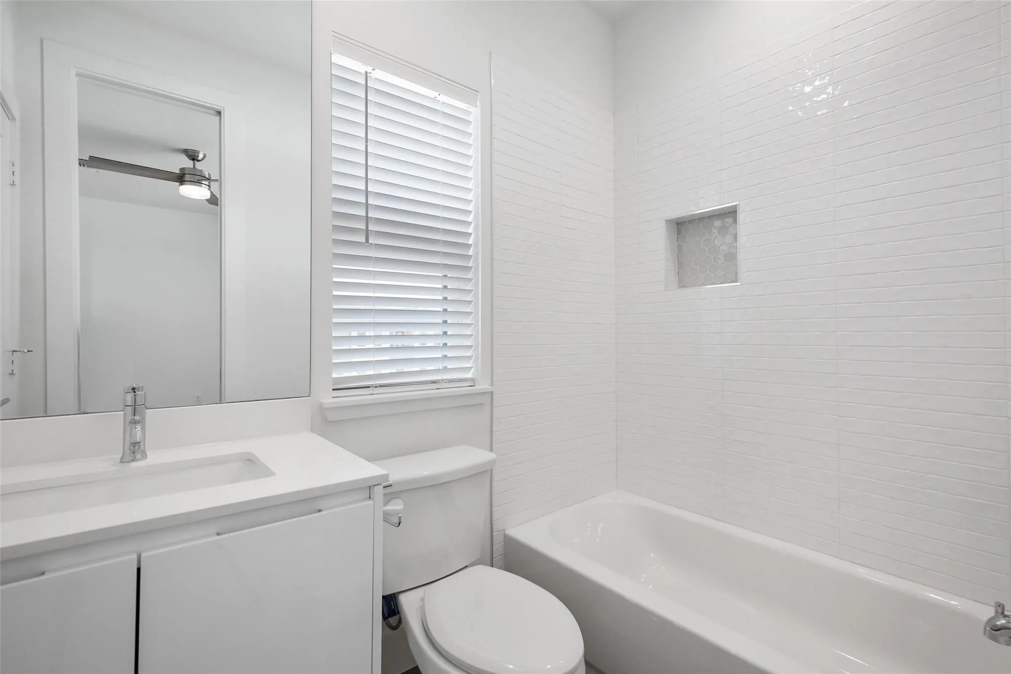 White tile bath surround with recessed niche, built-in bathtub, white vanity with integrated sink, and polished chrome faucet