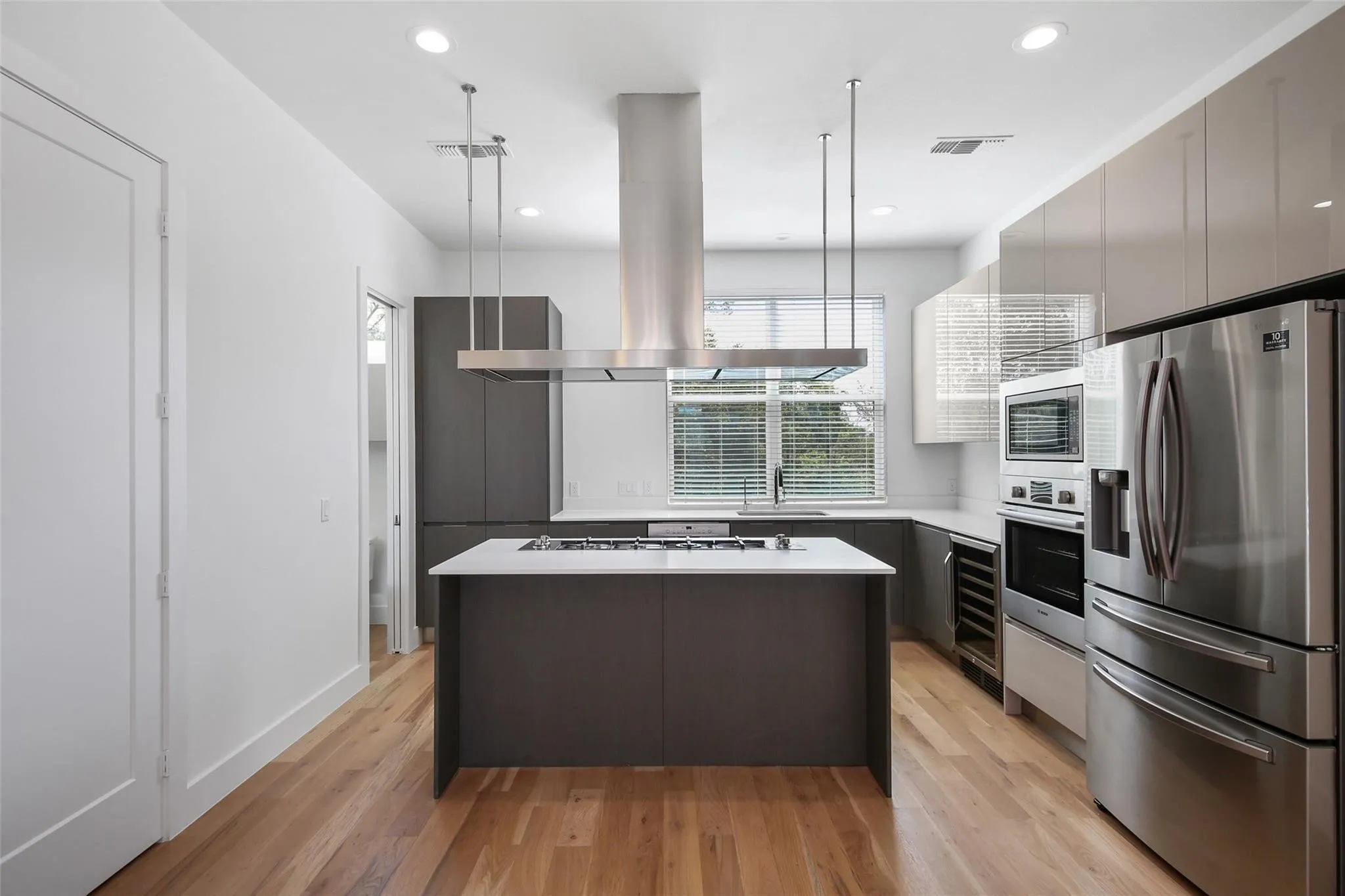 Modern kitchen featuring stainless steel appliances, a central island with cooktop, wood-finish flooring, recessed lighting, and ample cabinet storage
