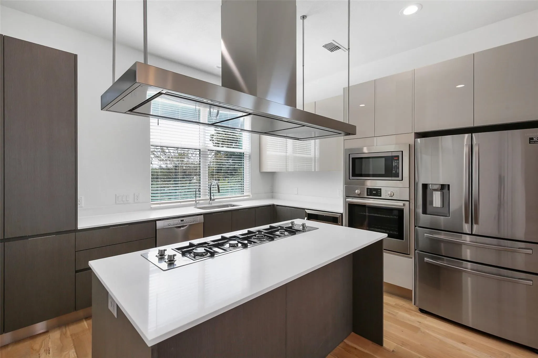 Modern kitchen featuring stainless steel appliances, a center island with a gas cooktop, sleek flat-panel cabinetry, and wood-finish flooring