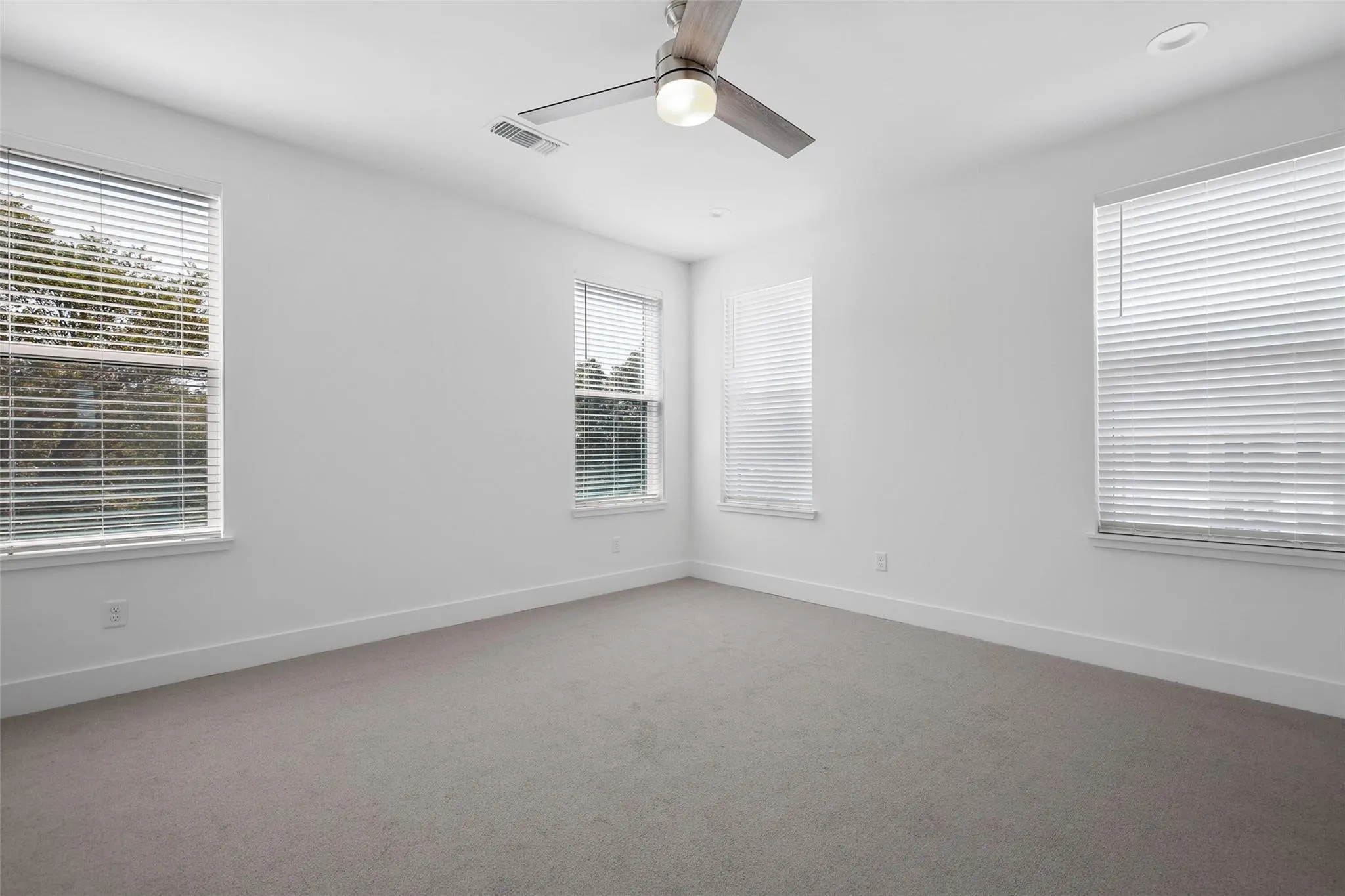 Walls with a neutral paint palette, recessed ceiling light, ceiling fan with light, three windows with horizontal blinds, and carpeting