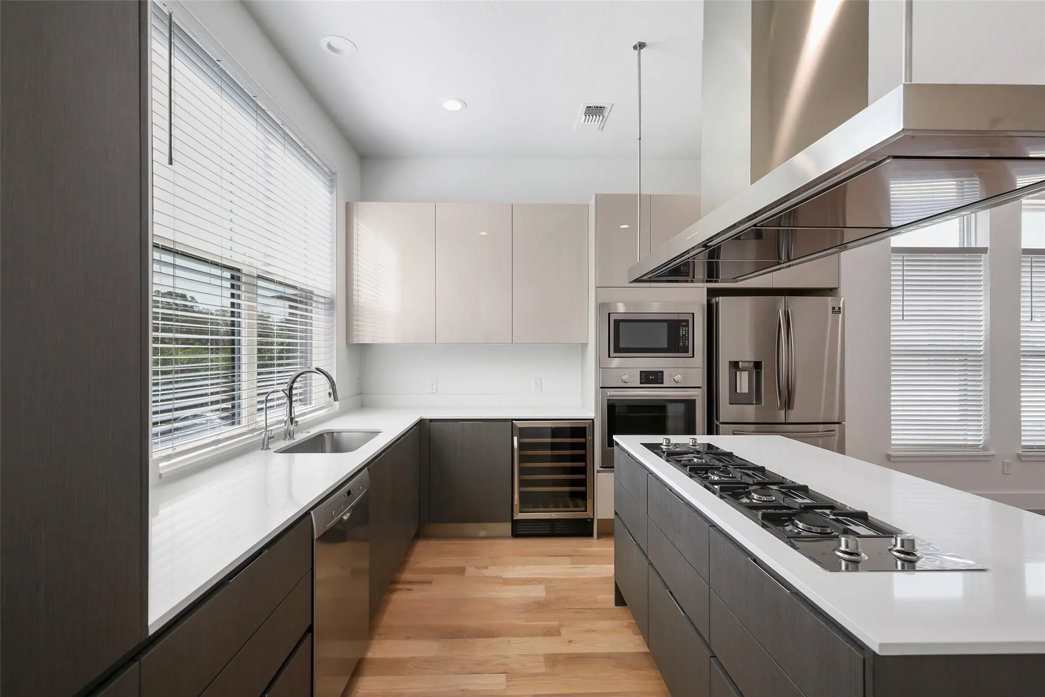 Modern kitchen featuring wood-finish flooring, stainless steel appliances, a center island with a gas cooktop, and a built-in wine cooler