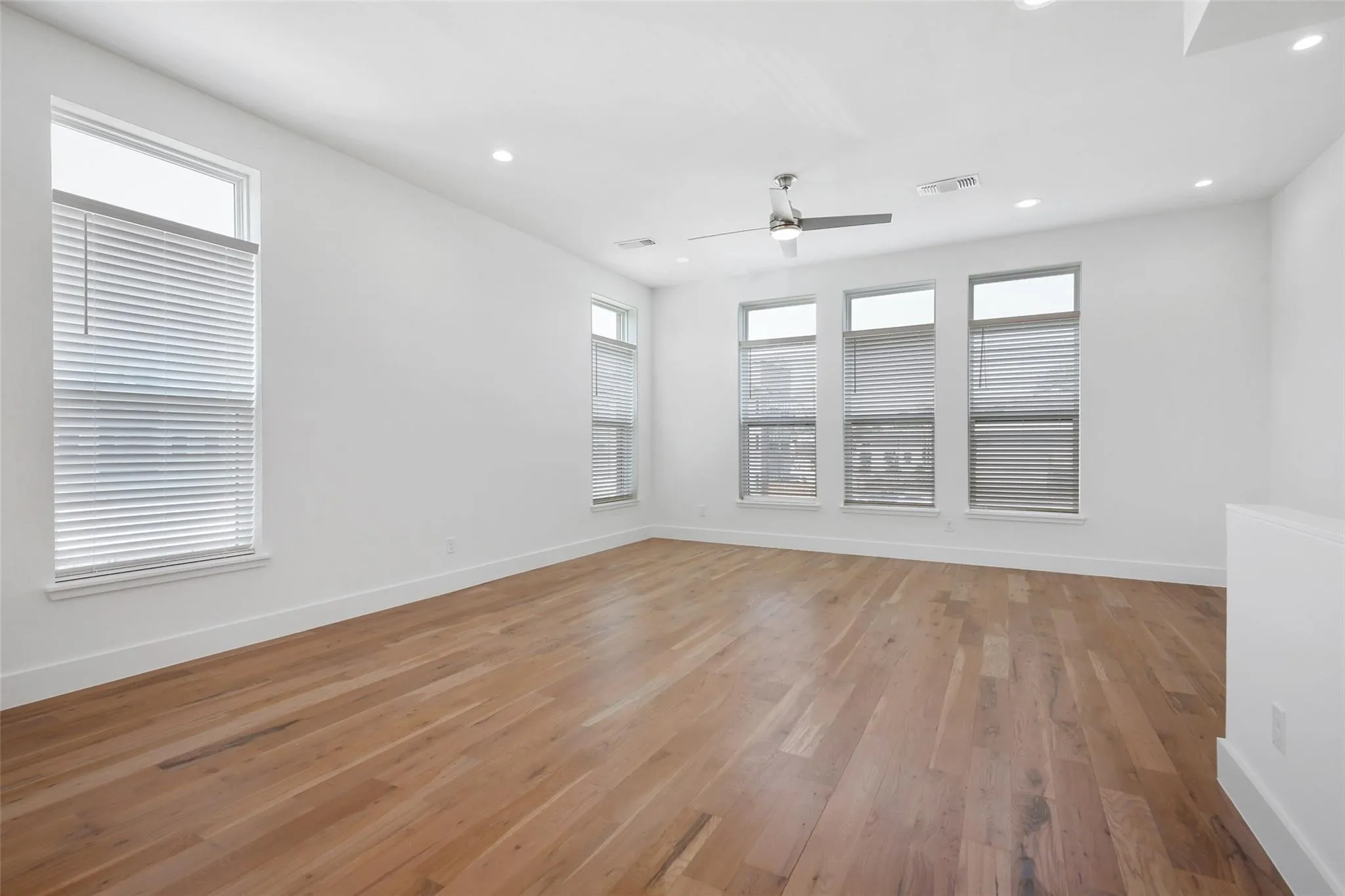Expansive room featuring wood-finish flooring, multiple windows, a ceiling fan, and recessed lighting