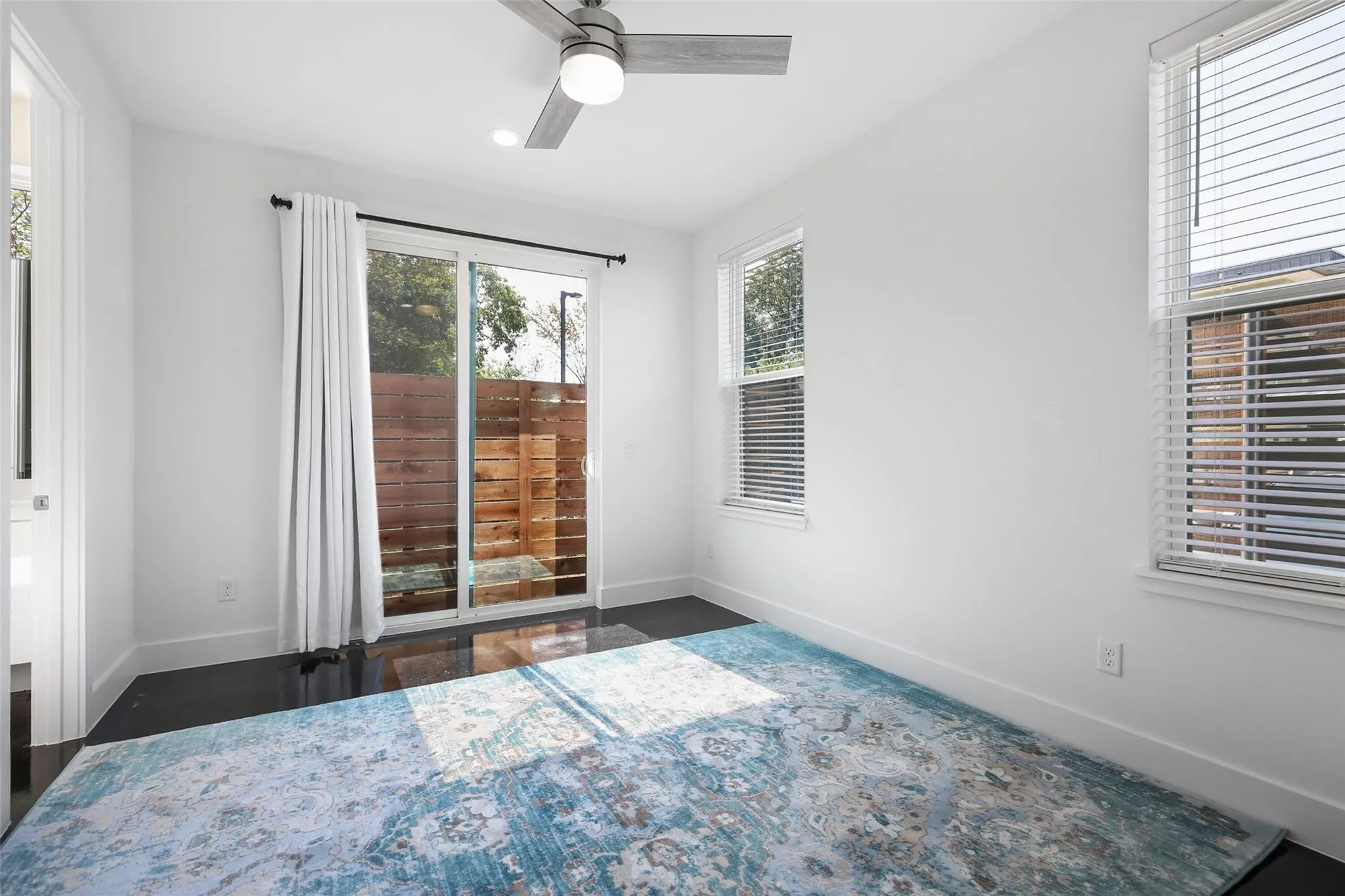 Recessed lighting, ceiling fan with light fixture, sliding glass door, multiple windows with blinds, and dark flooring