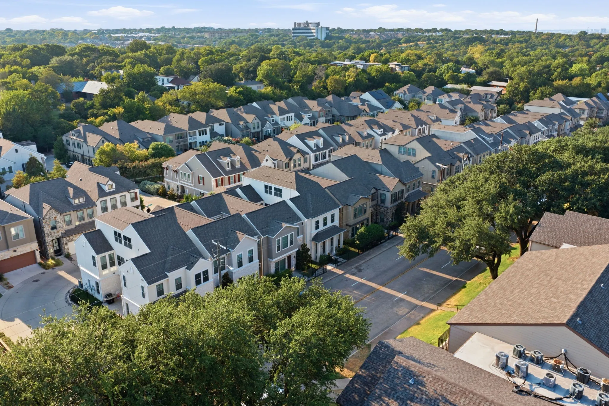 Residential street with mature trees and a collection of multi-story homes featuring varied architectural styles and roofing materials