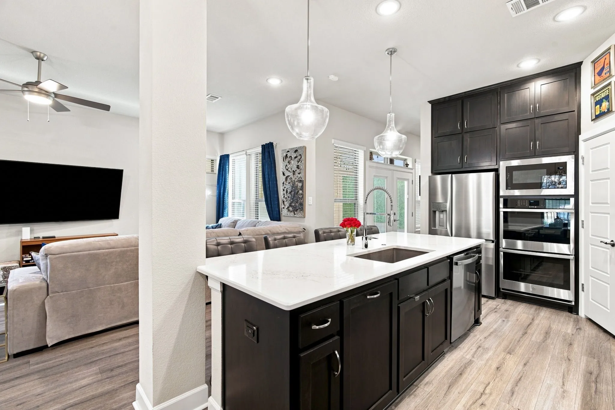 Kitchen island with an undermount sink, pendant lighting, dark cabinetry, stainless steel appliances, and light wood-finish flooring