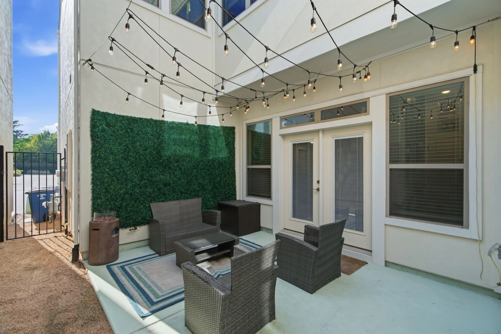 Paved outdoor patio with strung overhead lighting, double French doors, large windows, and a decorative green panel accent