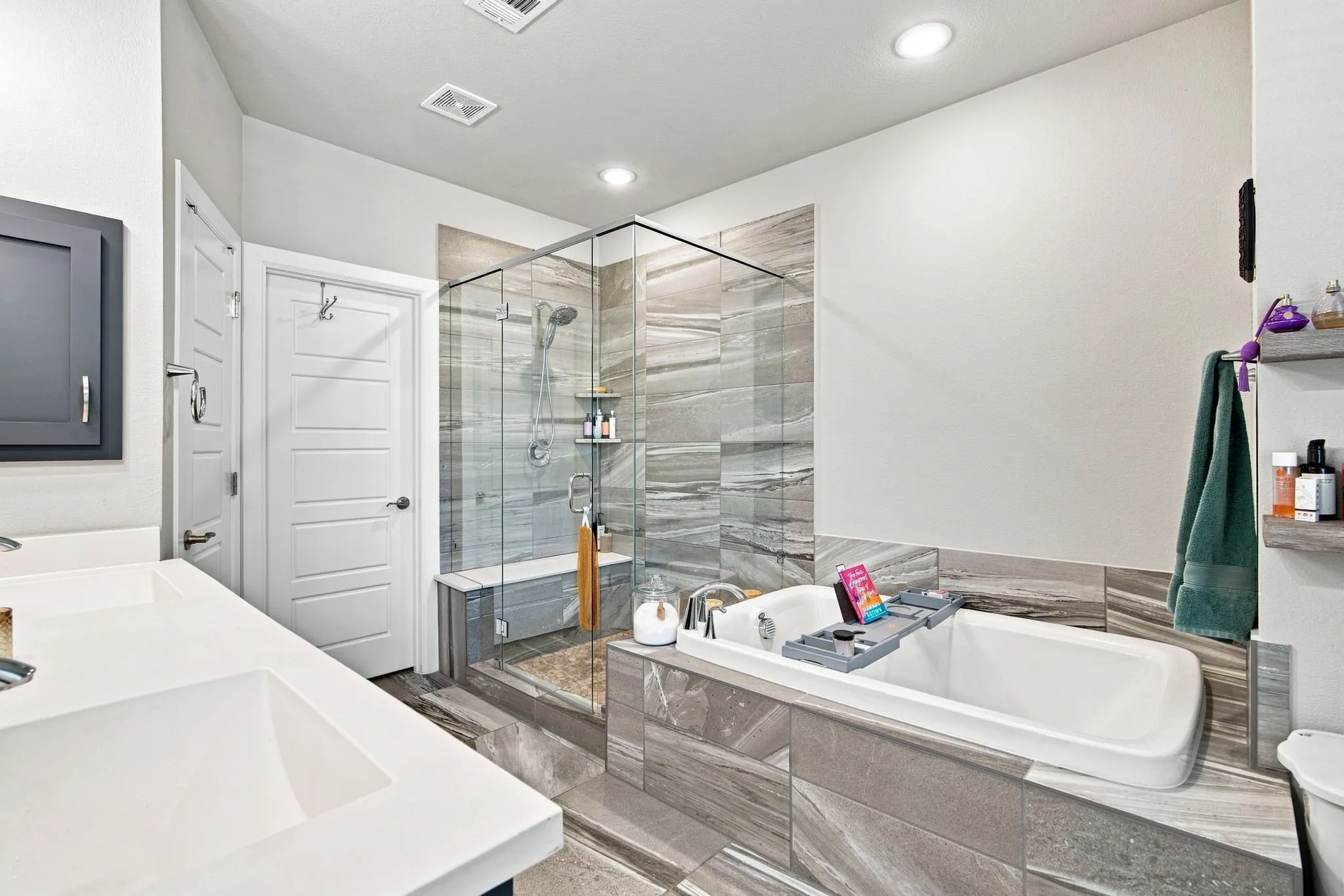 Dual vanity with integrated sinks, frameless glass shower enclosure with bench seating, soaking tub, and tile-surround walls