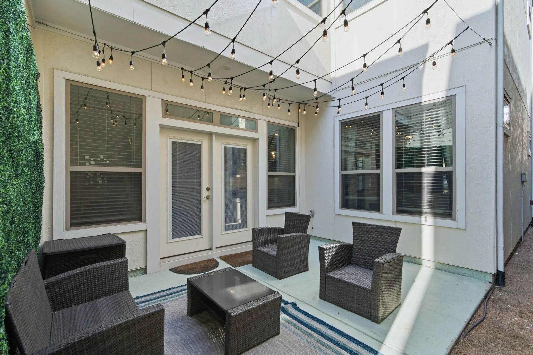 Private patio area featuring string lights, a textured privacy wall, and direct access through a double glass door