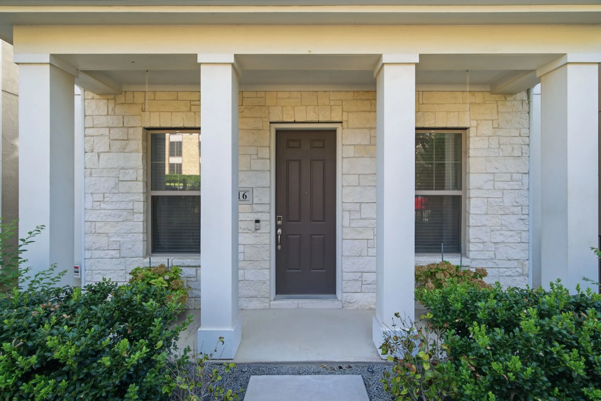 Covered entry with stone veneer facade, dark wood-finish door, and white columns