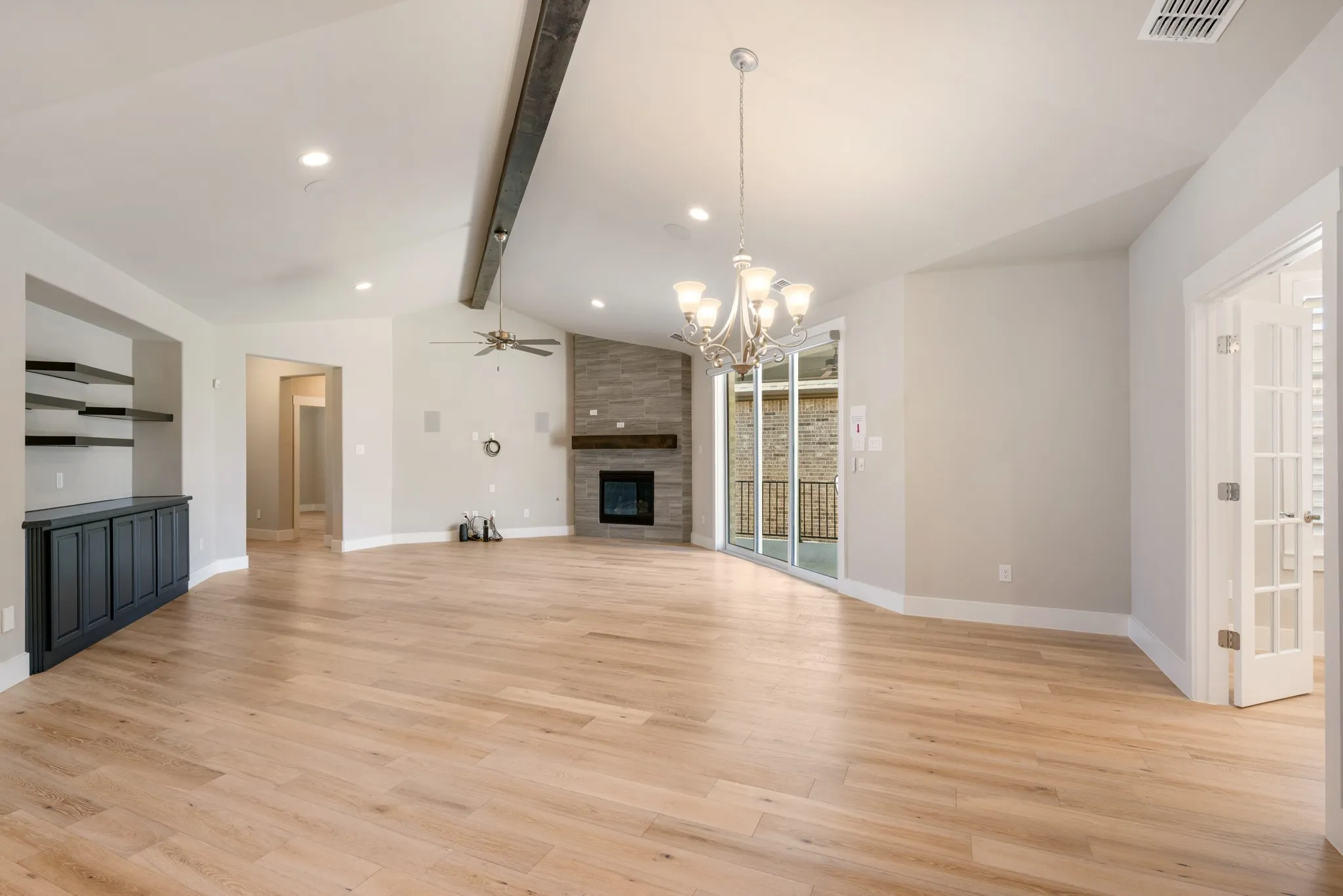 Spacious and inviting living area featuring vaulted ceilings, an exposed wood beam, and a stylish tiled fireplace with wood mantel. Abundant natural light fills the open space, complemented by luxury wood-look flooring.