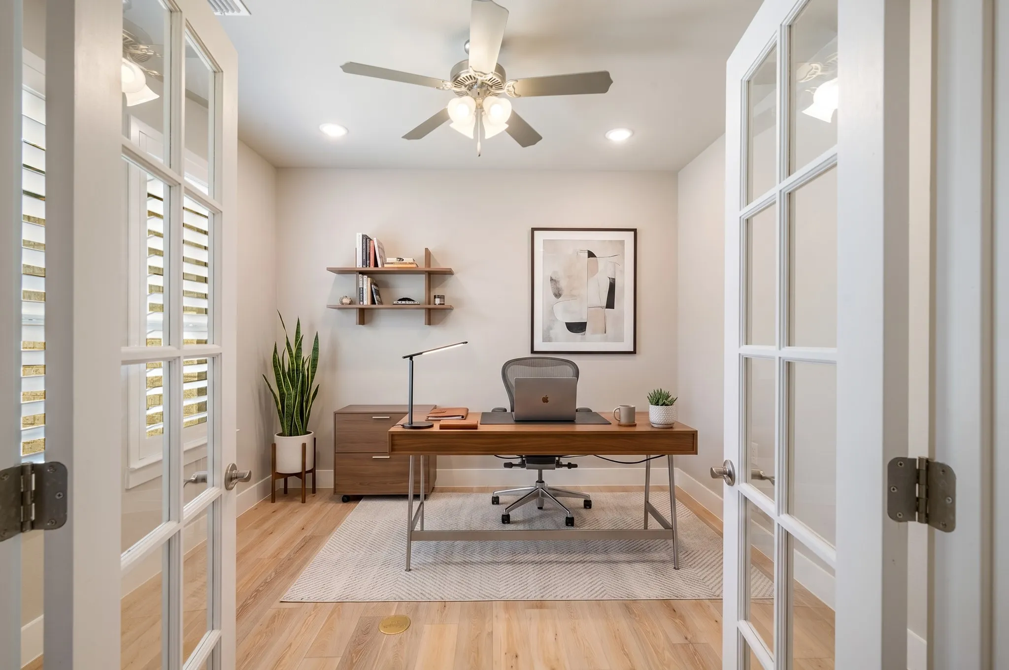Versatile home office featuring French doors, wood-look flooring, built-in style shelving, and a ceiling fan with light. The thoughtfully designed space offers a comfortable and private setting for working from home, studying, or managing daily tasks. Virtually staged.
