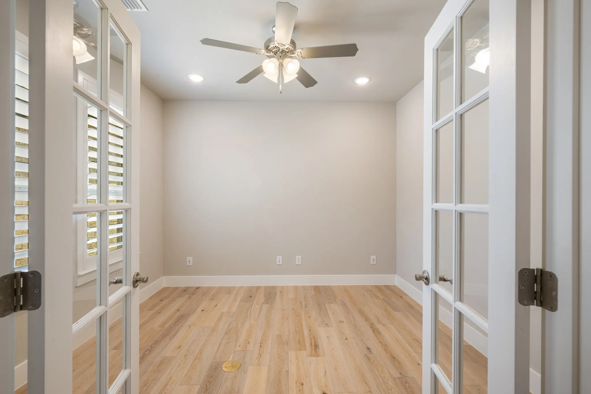 Versatile home office featuring French doors, wood-look flooring, built-in style shelving, and a ceiling fan with light. The thoughtfully designed space offers a comfortable and private setting for working from home, studying, or managing daily tasks.