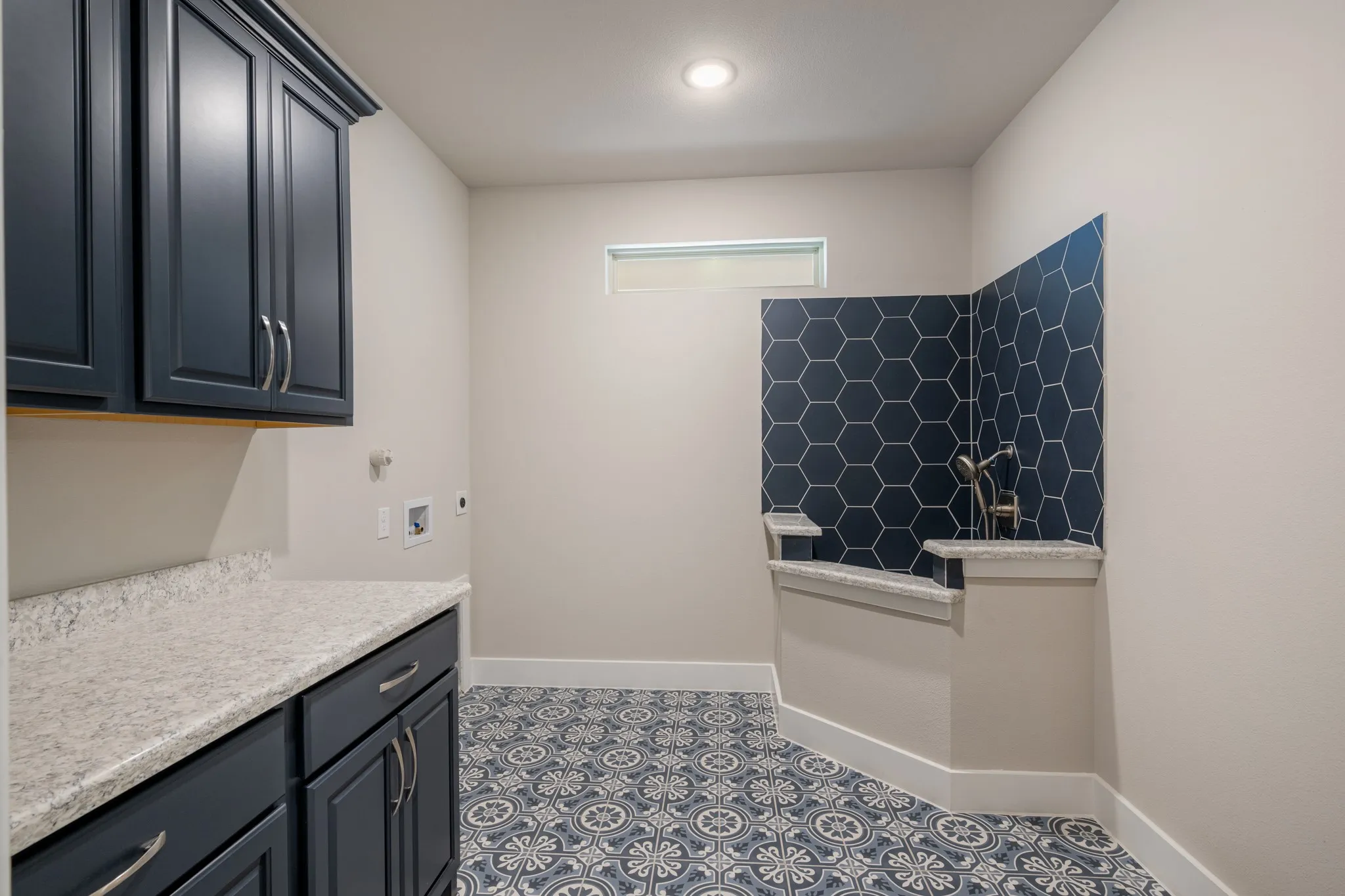 Spacious laundry room featuring abundant cabinetry, granite countertops, a pet wash center, and convenient washer and dryer connections. Decorative patterned tile flooring and a striking hexagon tile accent add a stylish touch to this functional space.