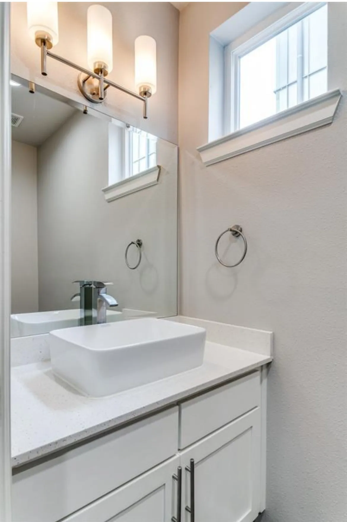 Vanity with a white vessel sink, polished chrome faucet, white cabinetry, and light-toned countertop