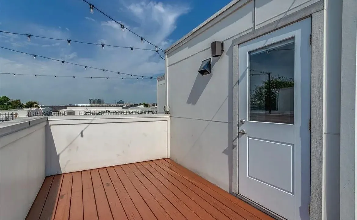 Rooftop deck featuring wood-finish flooring, white perimeter walls, and a white exterior door with an upper glass panel
