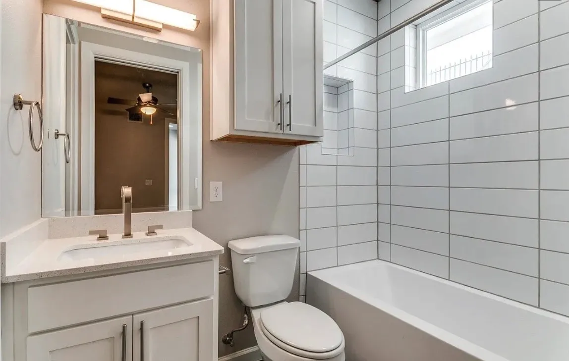 Bathroom featuring a white vanity with an undermount sink and light-toned countertop, a rectangular mirror, a bathtub with subway tile surround, and an integrated shower niche