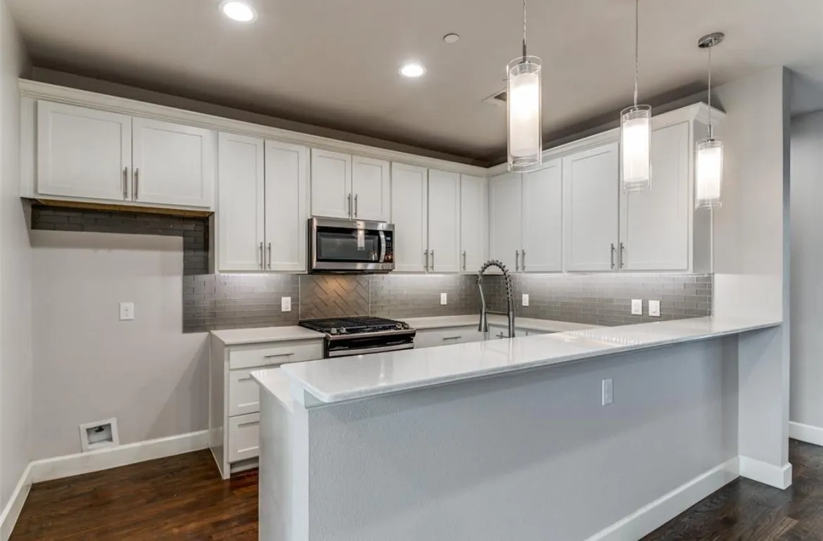 Kitchen featuring white shaker-style cabinetry, stainless steel appliances, a chevron tile backsplash, and a breakfast bar with pendant lighting