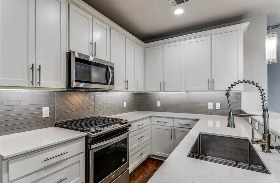 Kitchen featuring white shaker cabinetry, stainless steel appliances, light-colored countertops, a tile backsplash with a herringbone accent, and an undermount sink with a gooseneck faucet