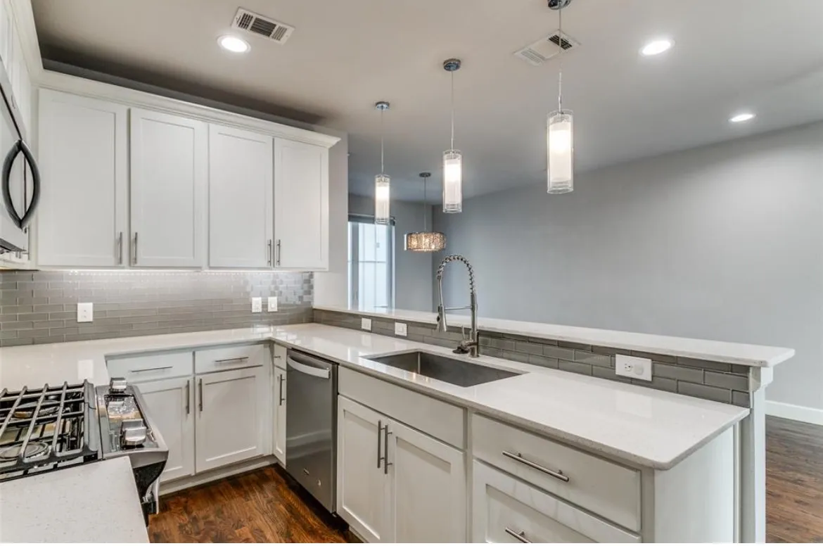 White shaker cabinetry with modern hardware, stainless steel appliances, quartz countertops, a gray subway tile backsplash, and wood-finish flooring
