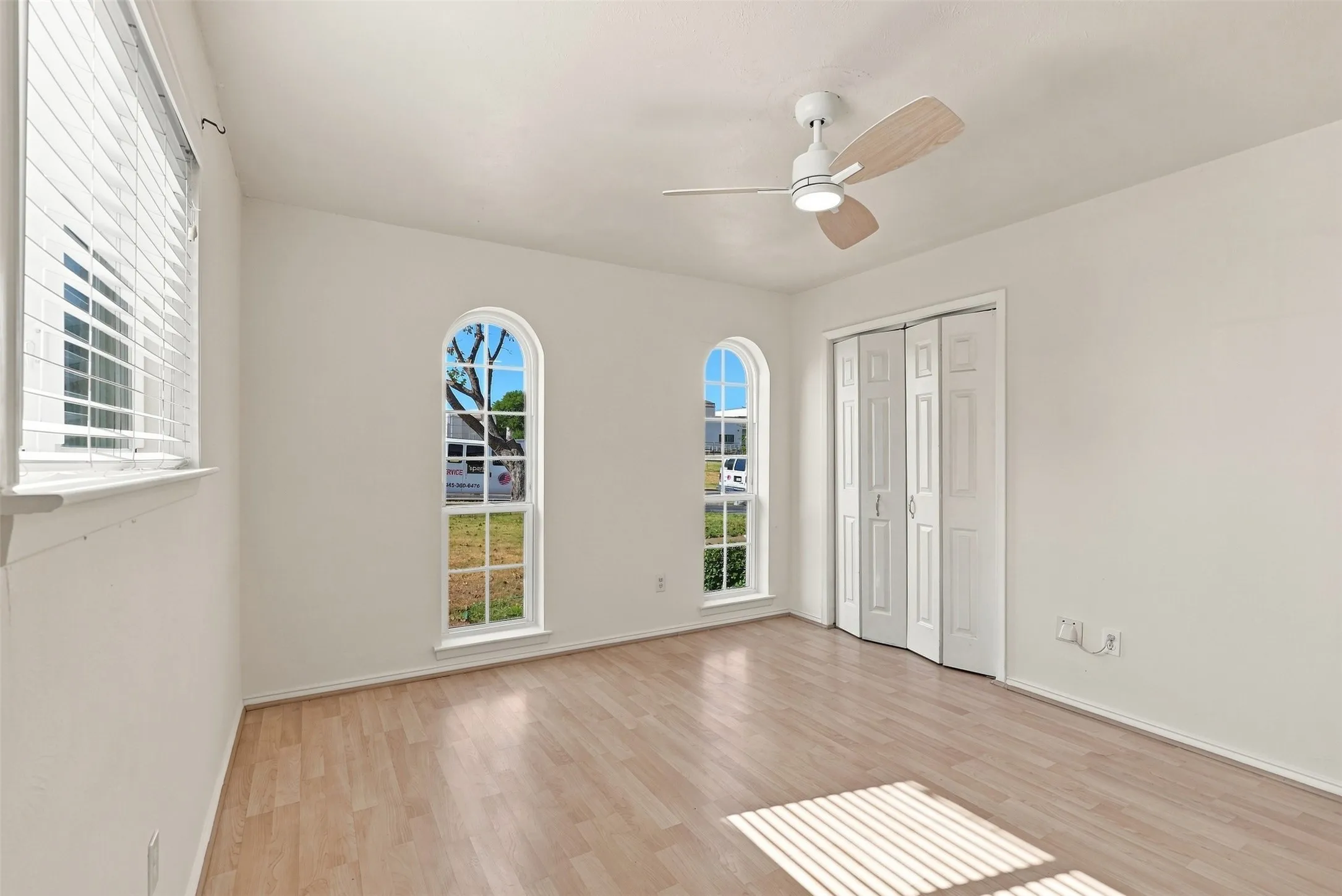 Light wood-finish flooring, arched windows, and a ceiling fan with light fixture
