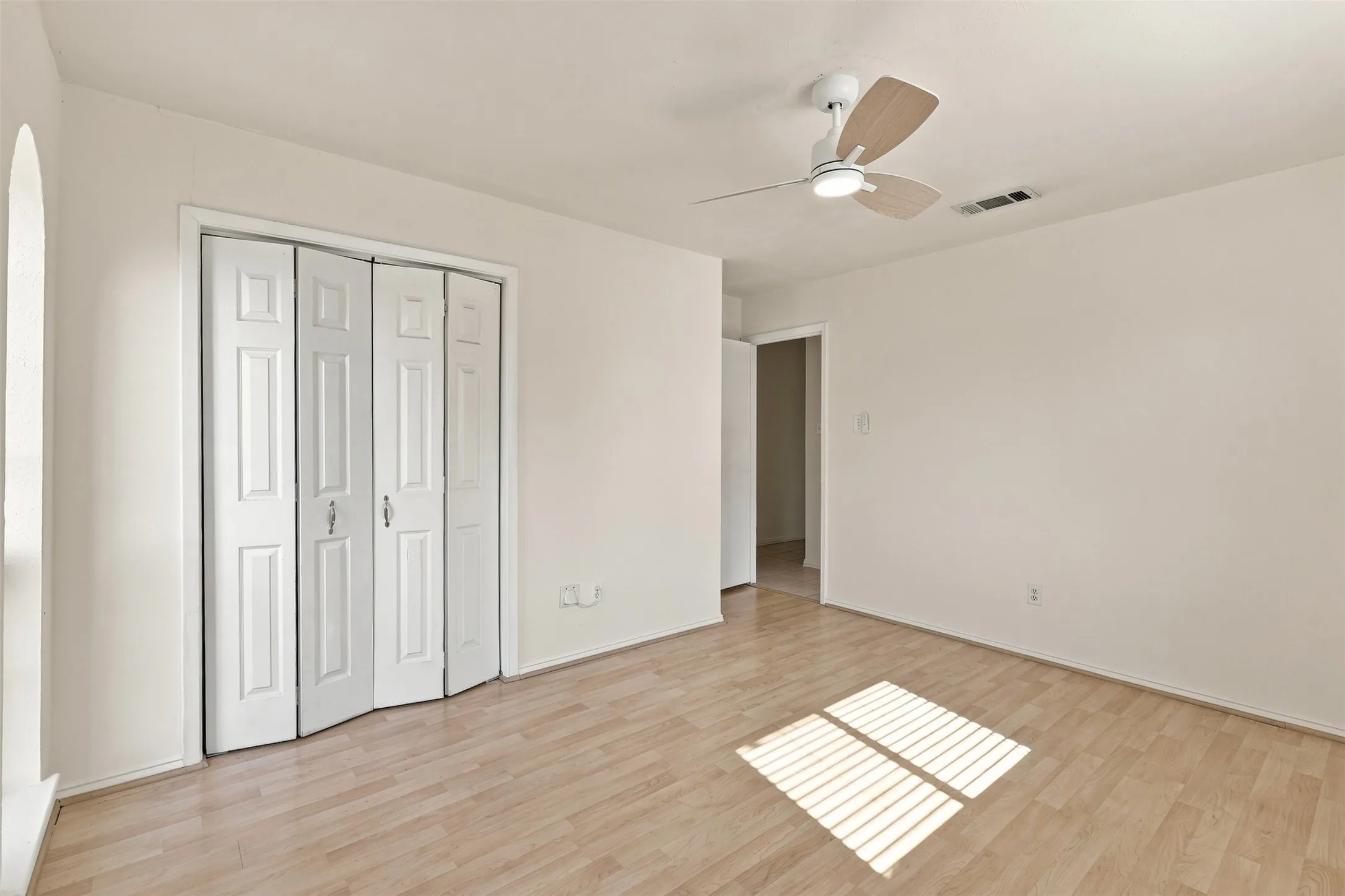 Wood-finish flooring, white walls, bi-fold closet doors, ceiling fan with integrated lighting, and an arched entryway