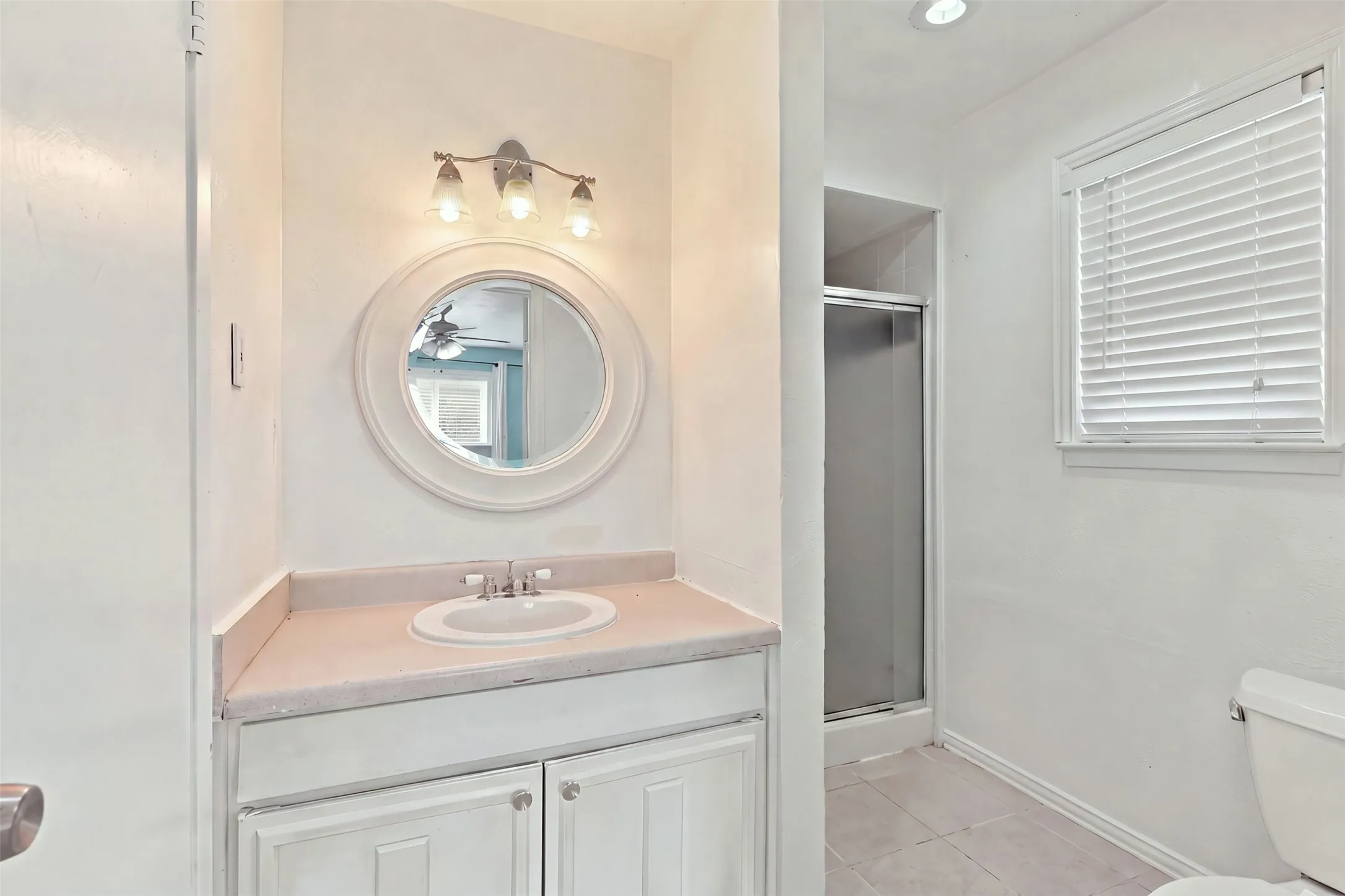 Vanity with an integrated sink, round mirror, three-light fixture, and shower stall with a glass enclosure
