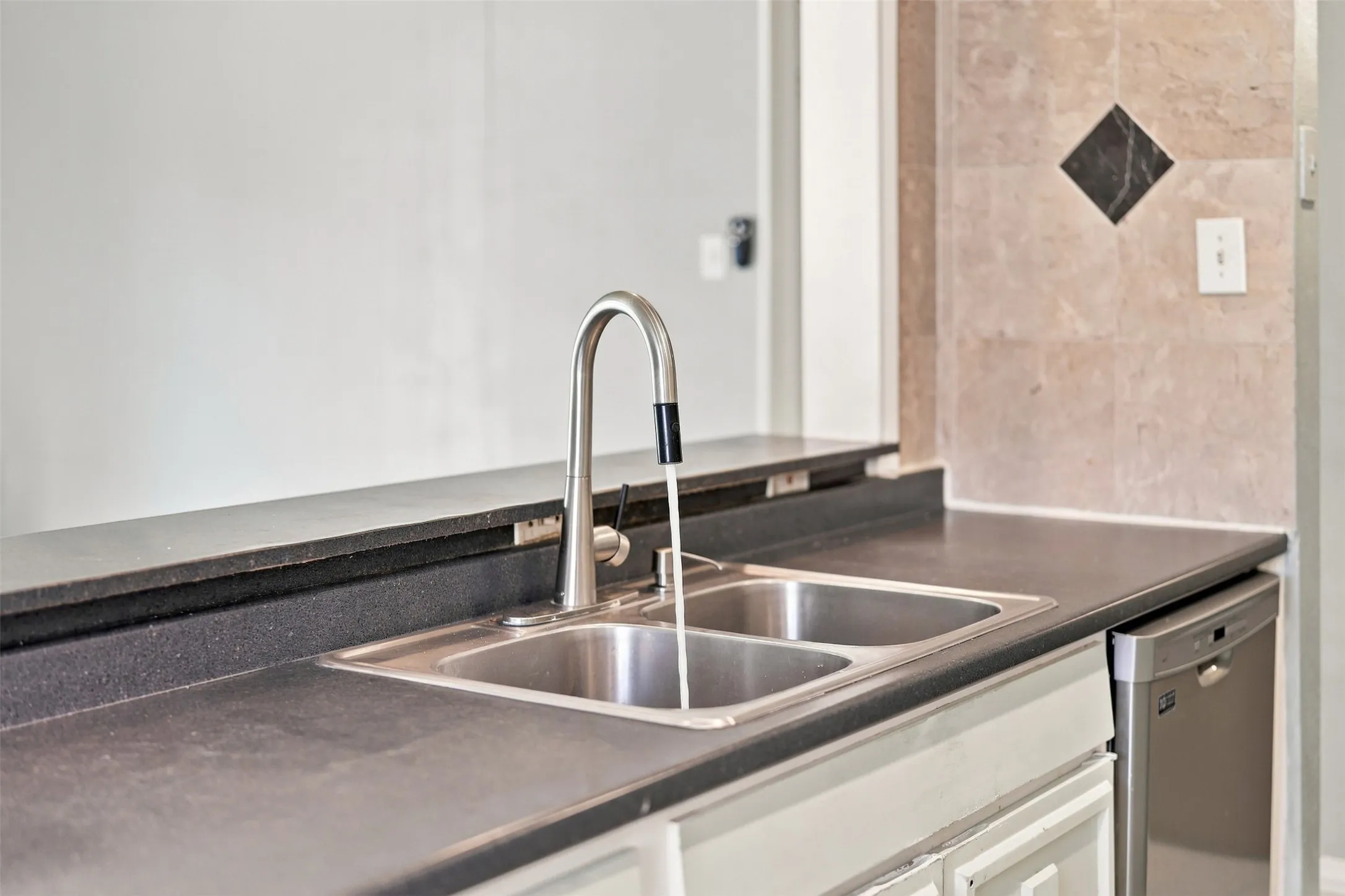 Dual basin stainless steel sink with a high-arc pull-down faucet, dark countertops, and a stainless steel dishwasher