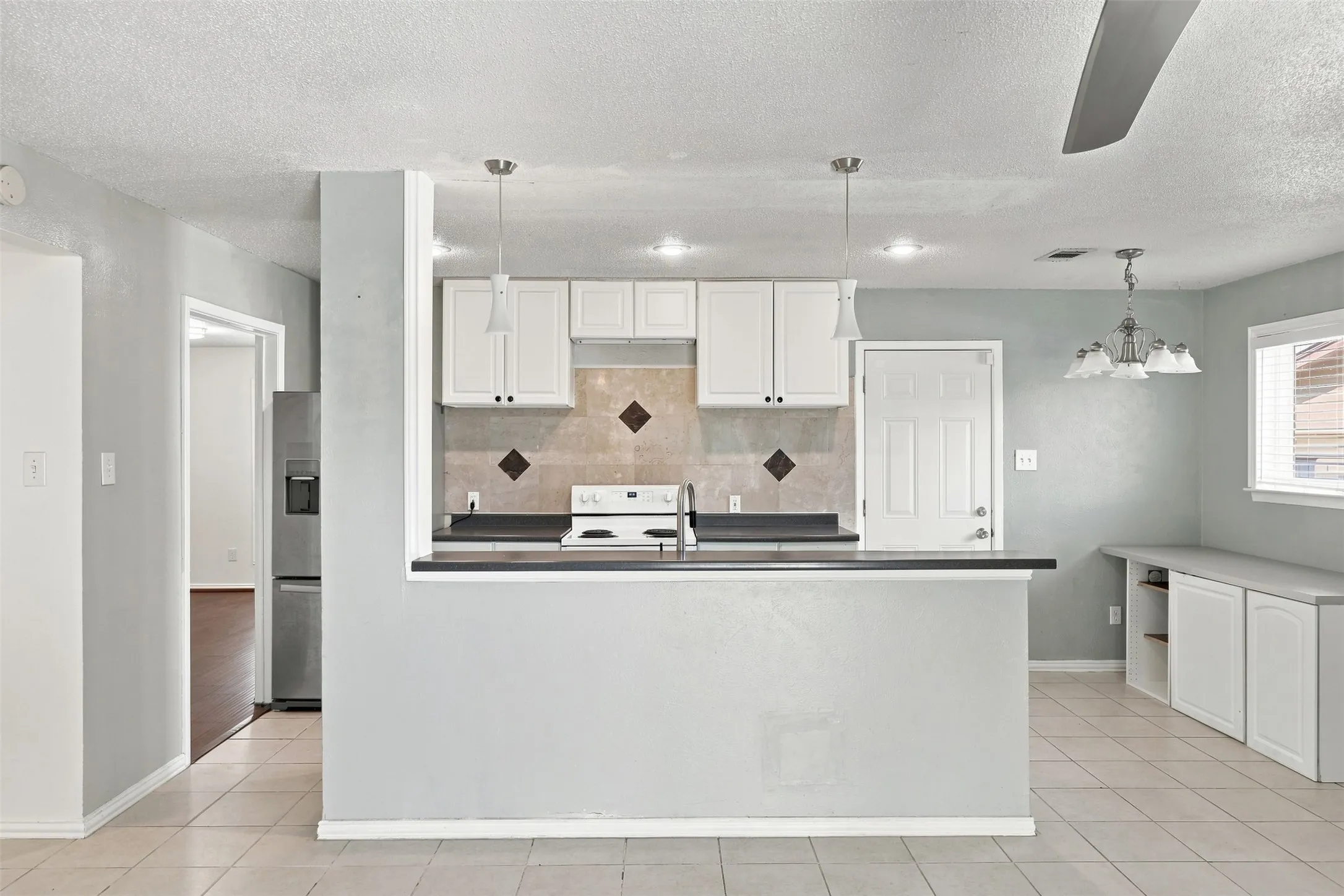 Kitchen featuring white cabinetry, tile backsplash with accent squares, black countertops, and a built-in range