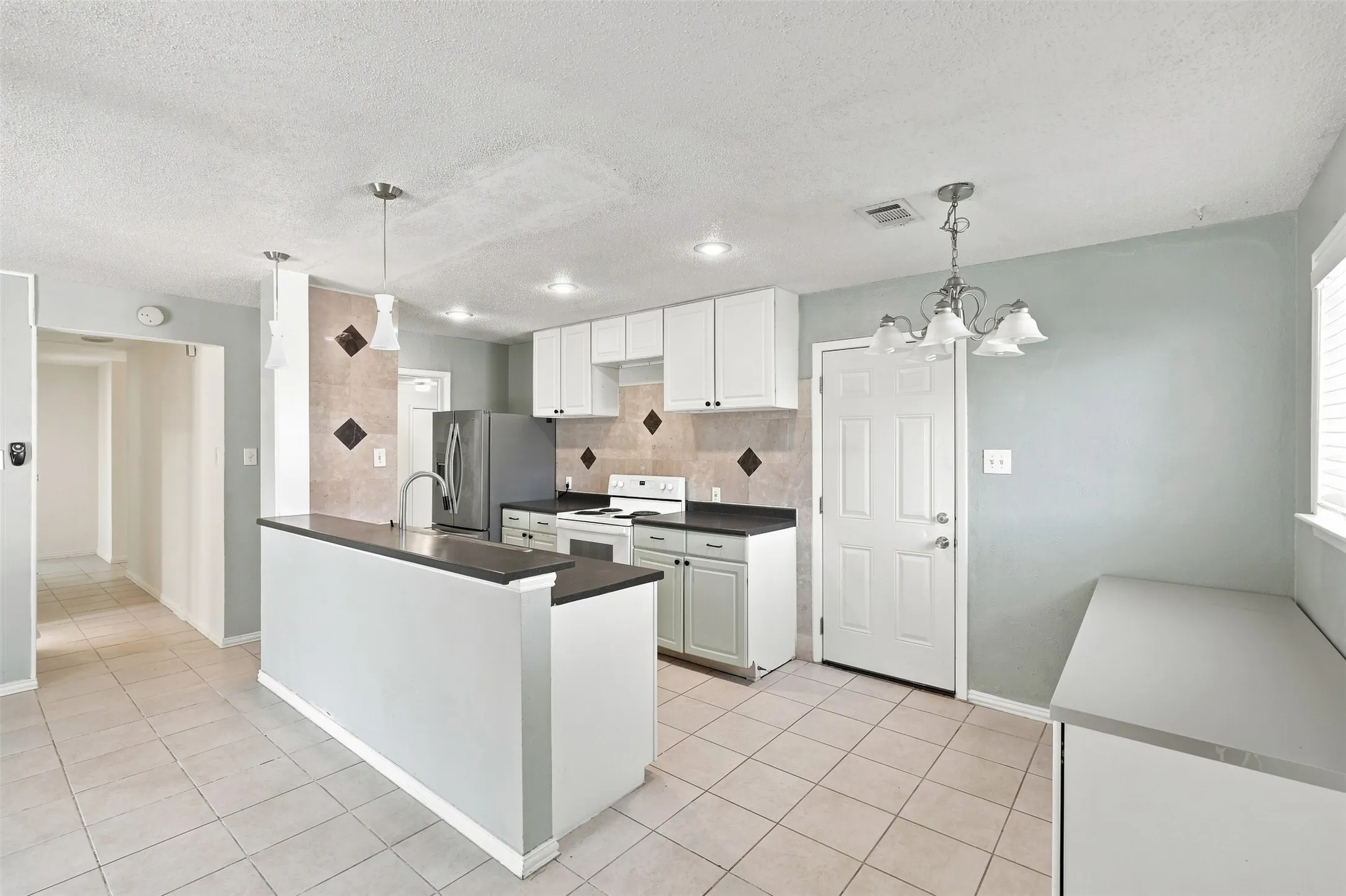 Kitchen featuring an island with a built-in sink, white cabinetry with dark hardware, a tile backsplash, and tile flooring