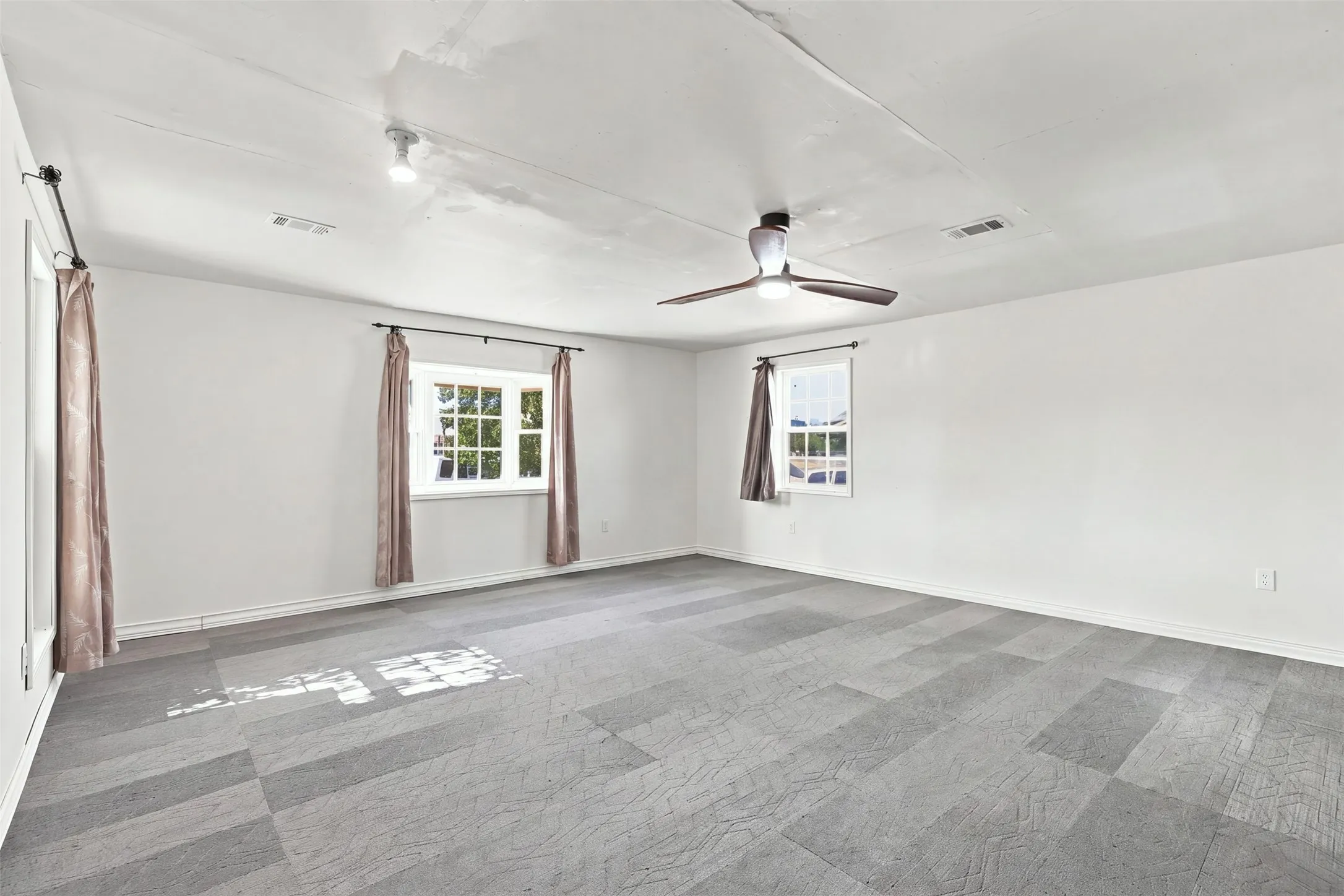 Spacious room featuring patterned carpet flooring, dual windows, a ceiling fan with integrated lighting, and track lighting