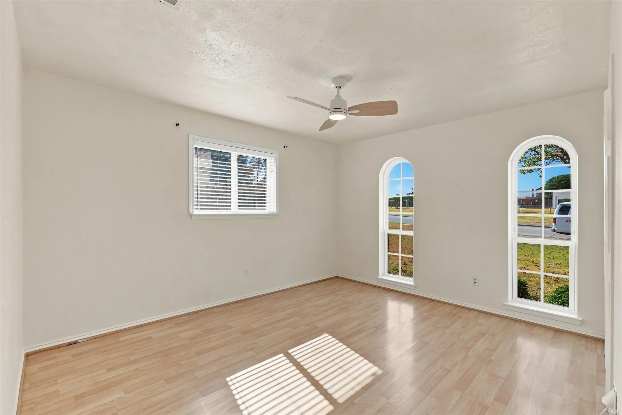 Vaulted ceiling with a ceiling fan, wood-finish flooring, and two arched windows