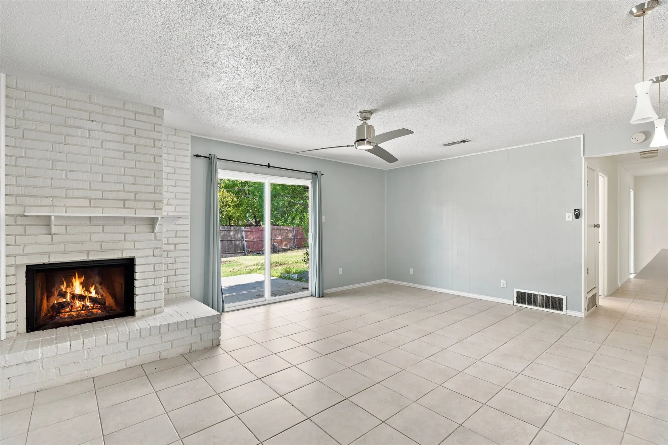 Brick fireplace with a mantel, ceramic tile flooring, sliding glass door, and a ceiling fan