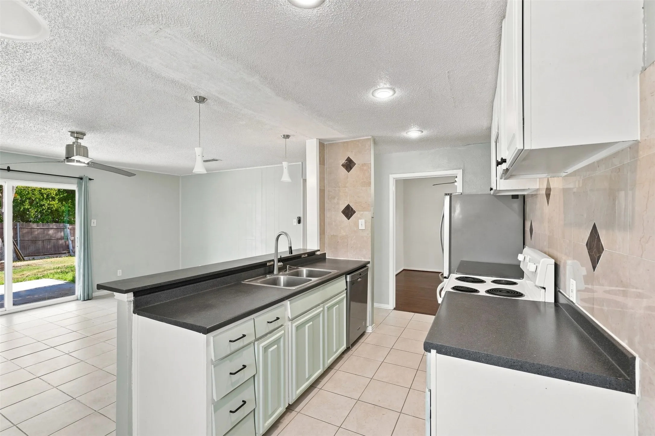 Kitchen featuring white cabinetry, dark countertops, a double basin sink, and a tile backsplash with diamond accents