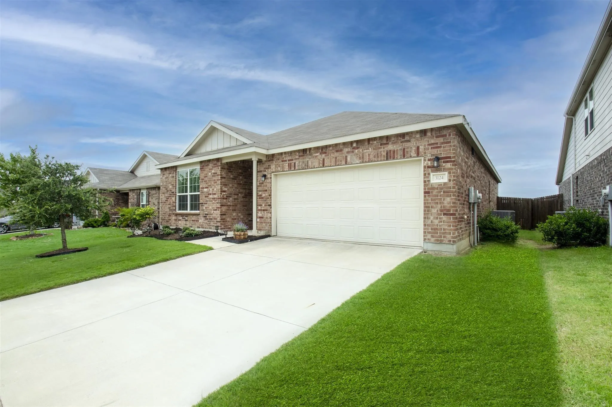 Brick exterior with white trim, attached garage, concrete driveway, and front landscaping