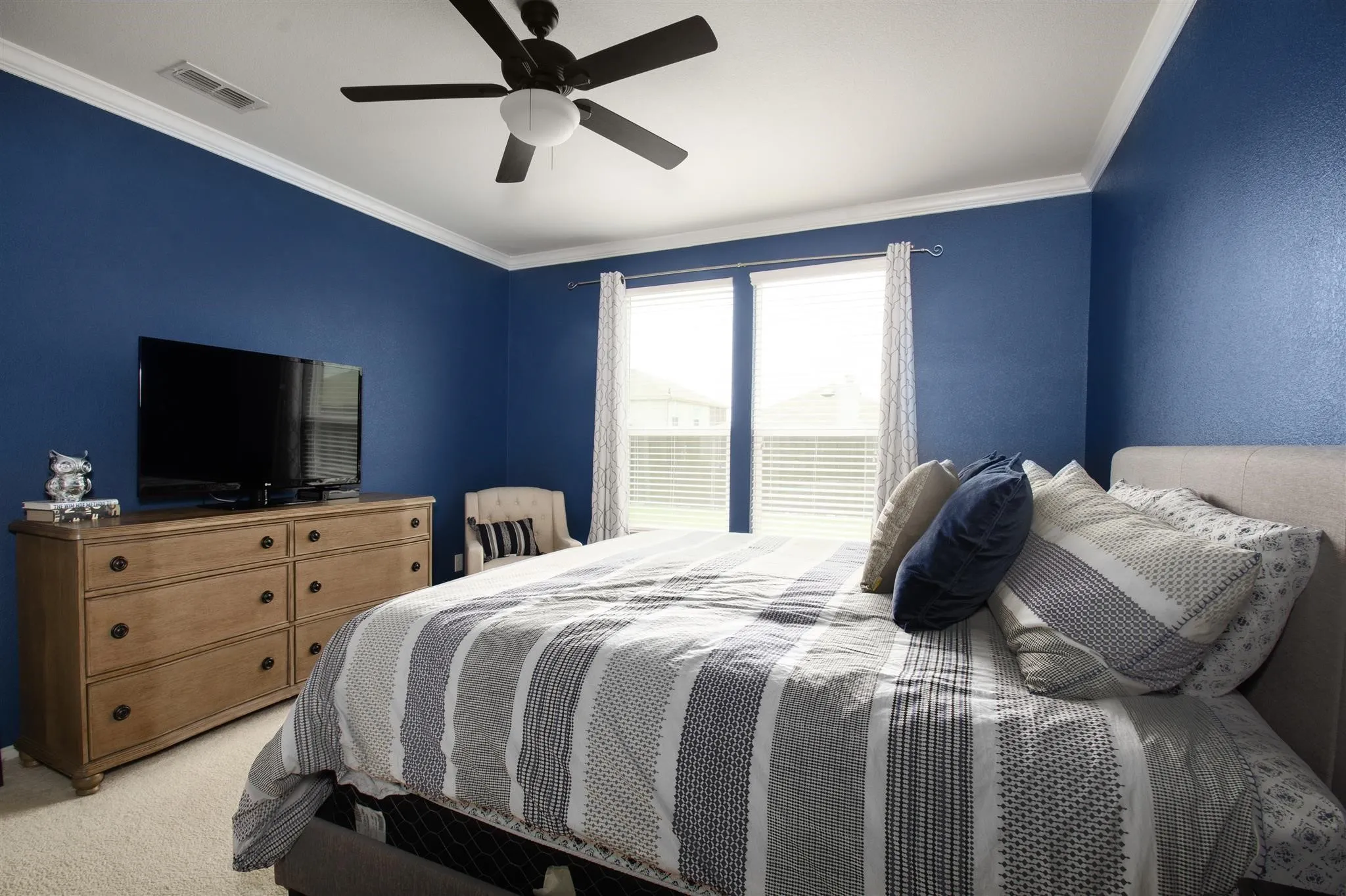 Crown molding, ceiling fan with integrated lighting, wood-finish dresser, and dual windows with blinds
