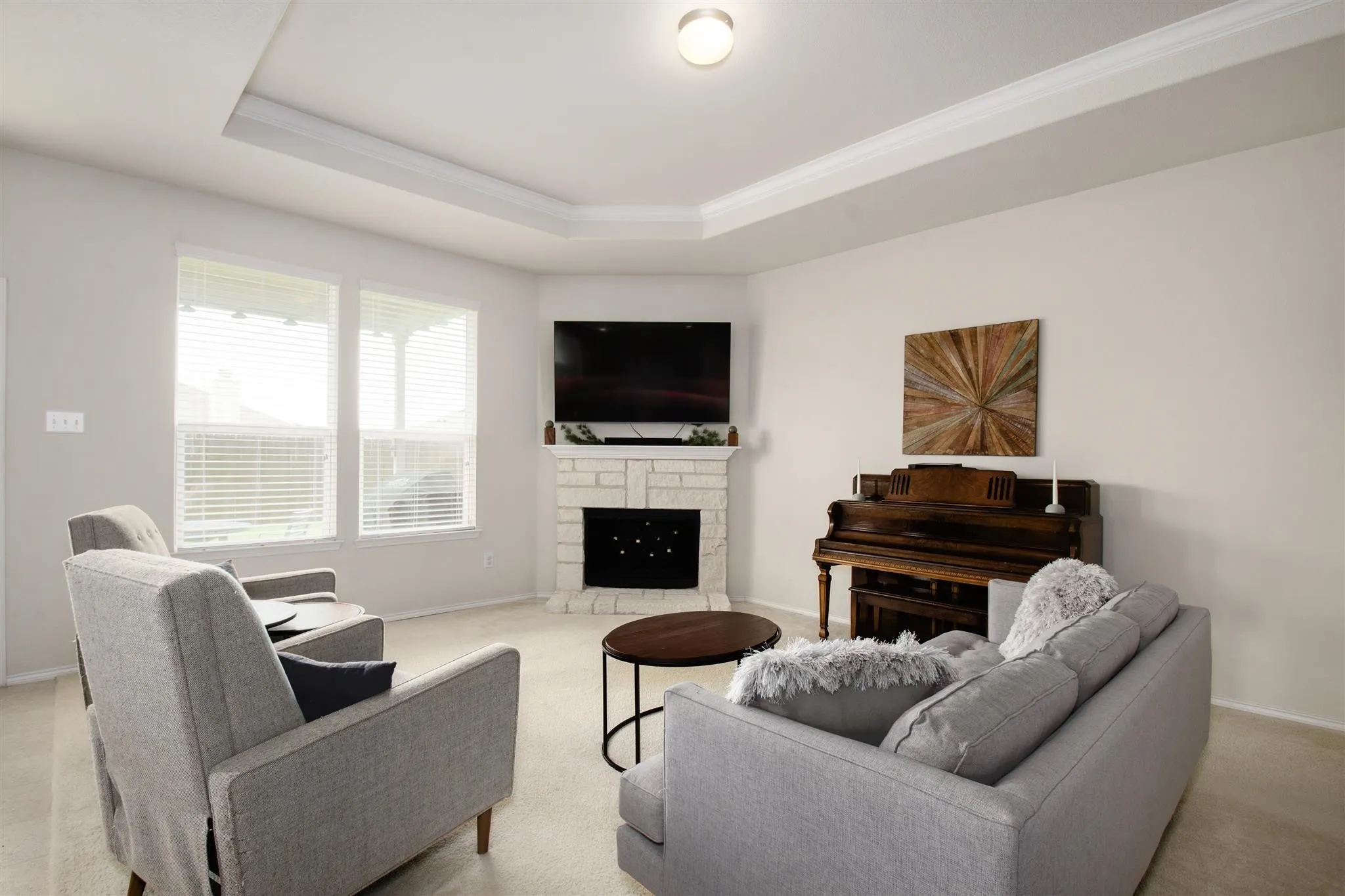 Tray ceiling with crown molding, corner fireplace with stone surround, recessed lighting, and large windows